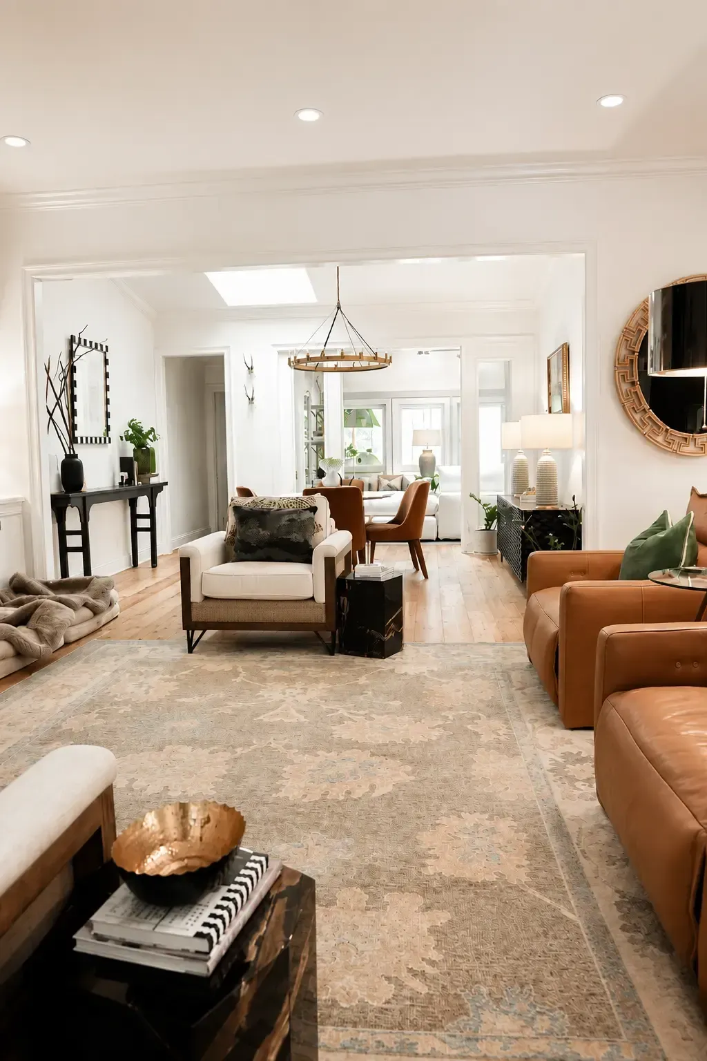 Bright living room with neutral decor, leather chairs, a rug, and a dining area by large windows.