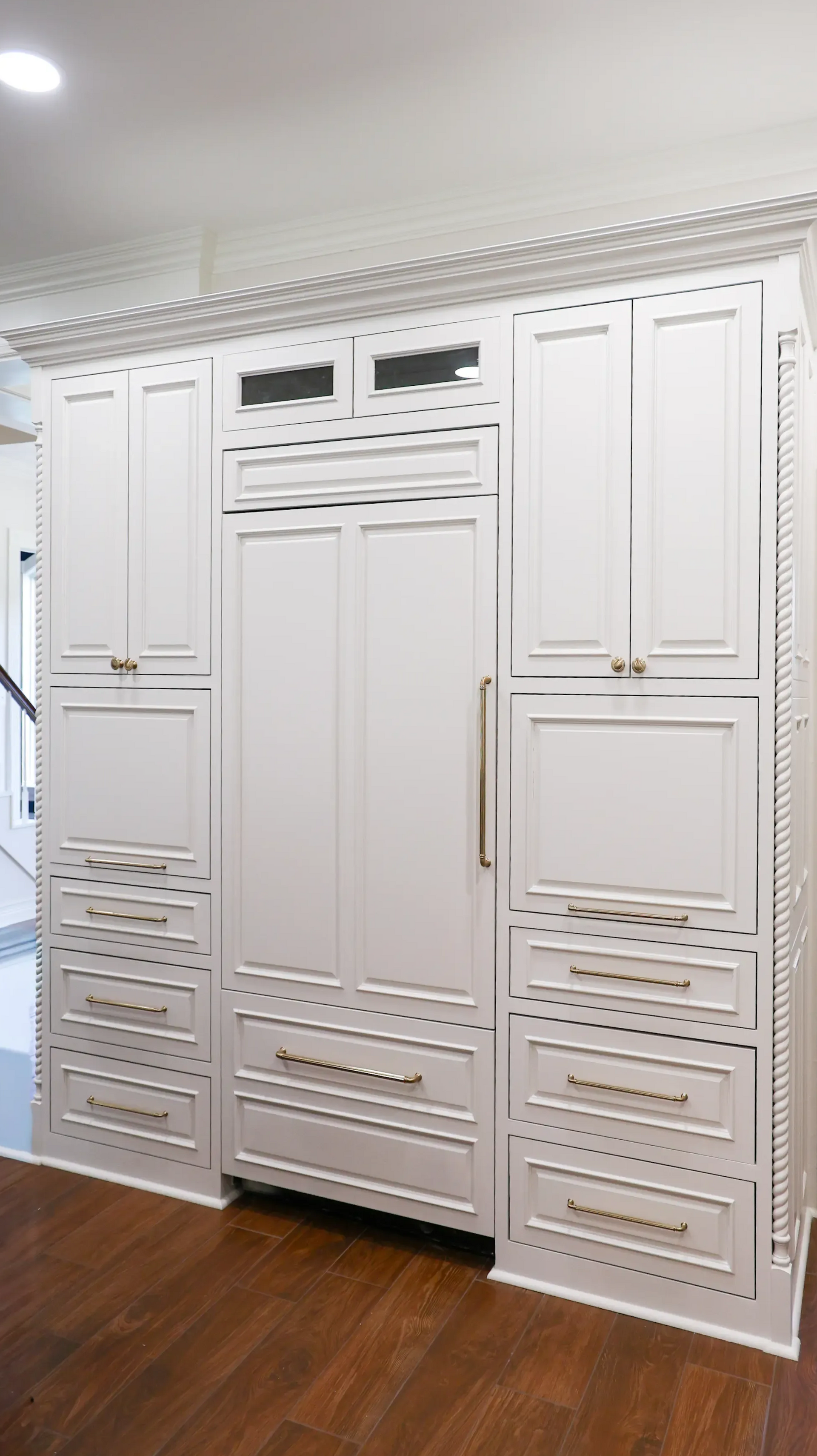 White built-in closet doors and drawers in a room with wood flooring and crown molding.