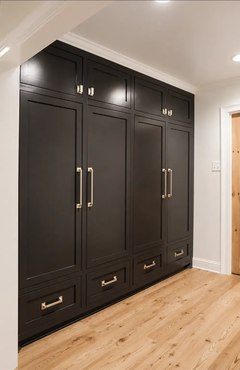 Built-in dark wood wardrobe with brass handles and drawers in a light hallway