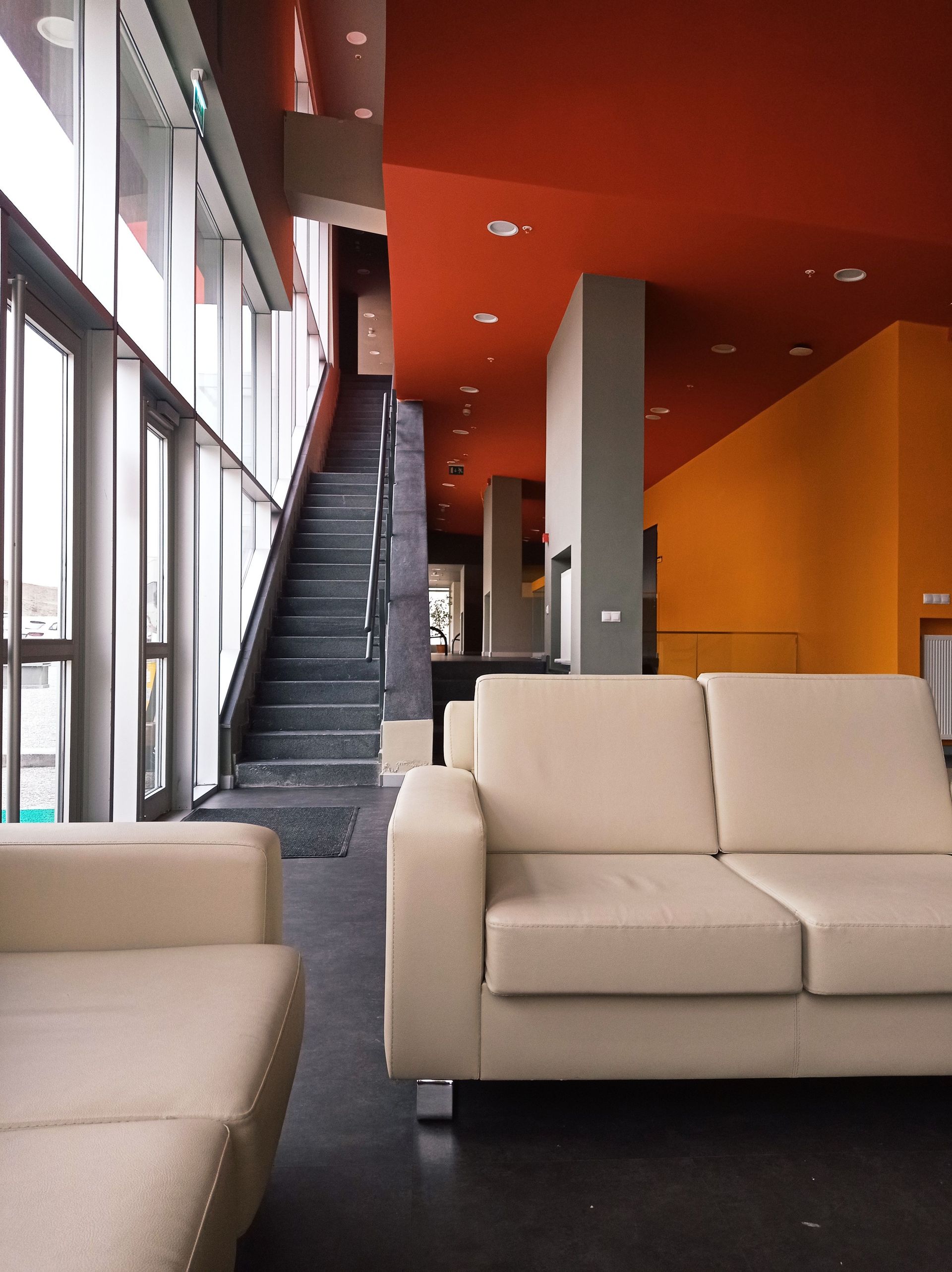 Modern lobby with beige sofas, a dark staircase, and orange-red walls and ceiling.