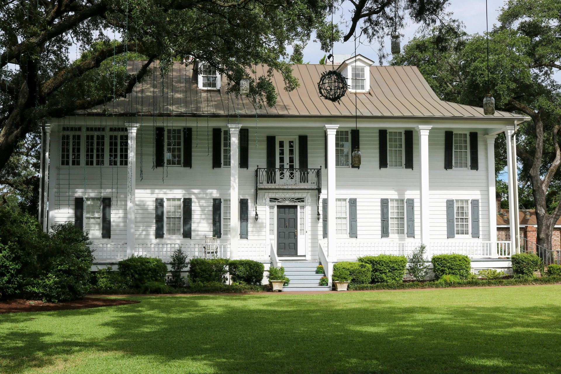White two-story colonial house with green shutters and a large front lawn under trees