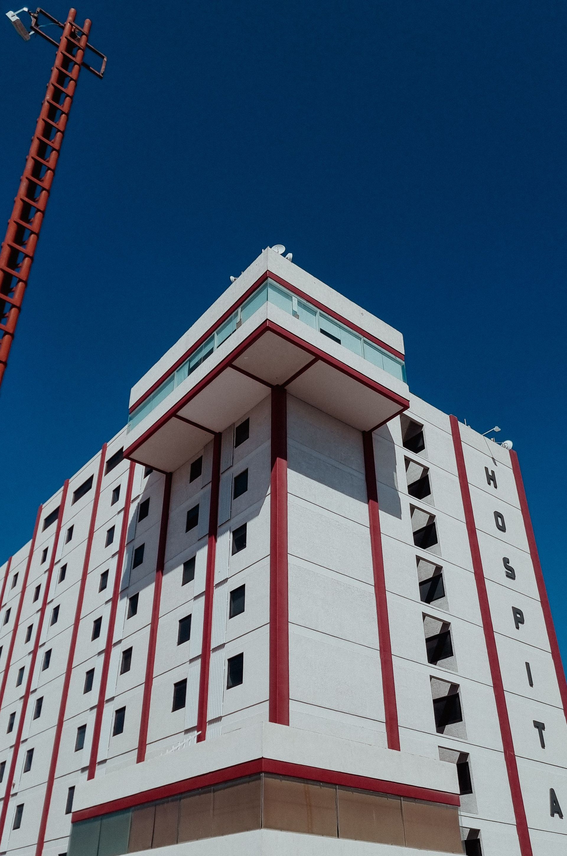 Tall white building with red trim under a clear blue sky, viewed from below; a crane rises at the left edge