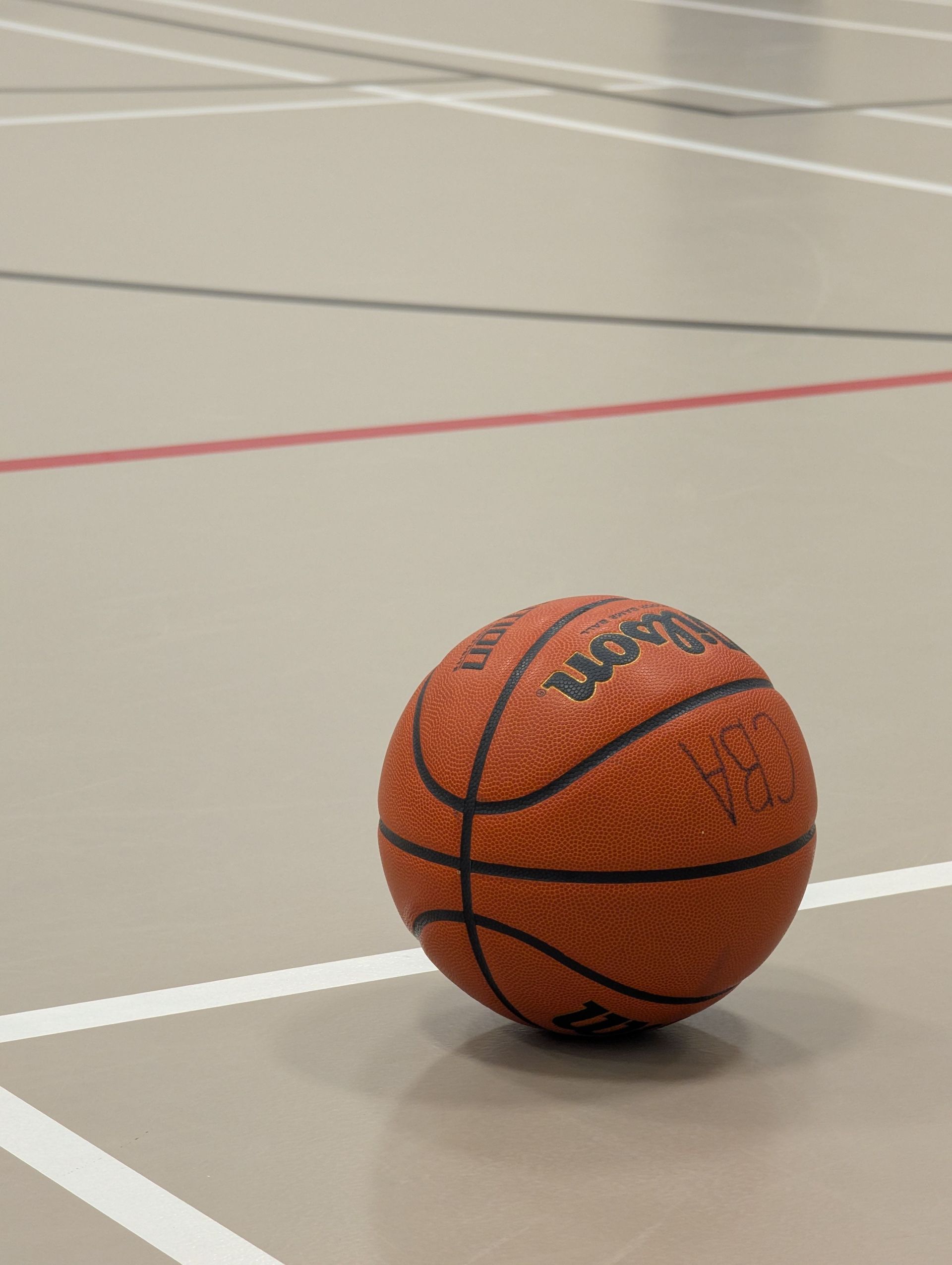 Basketball resting on an indoor court with white and red boundary lines