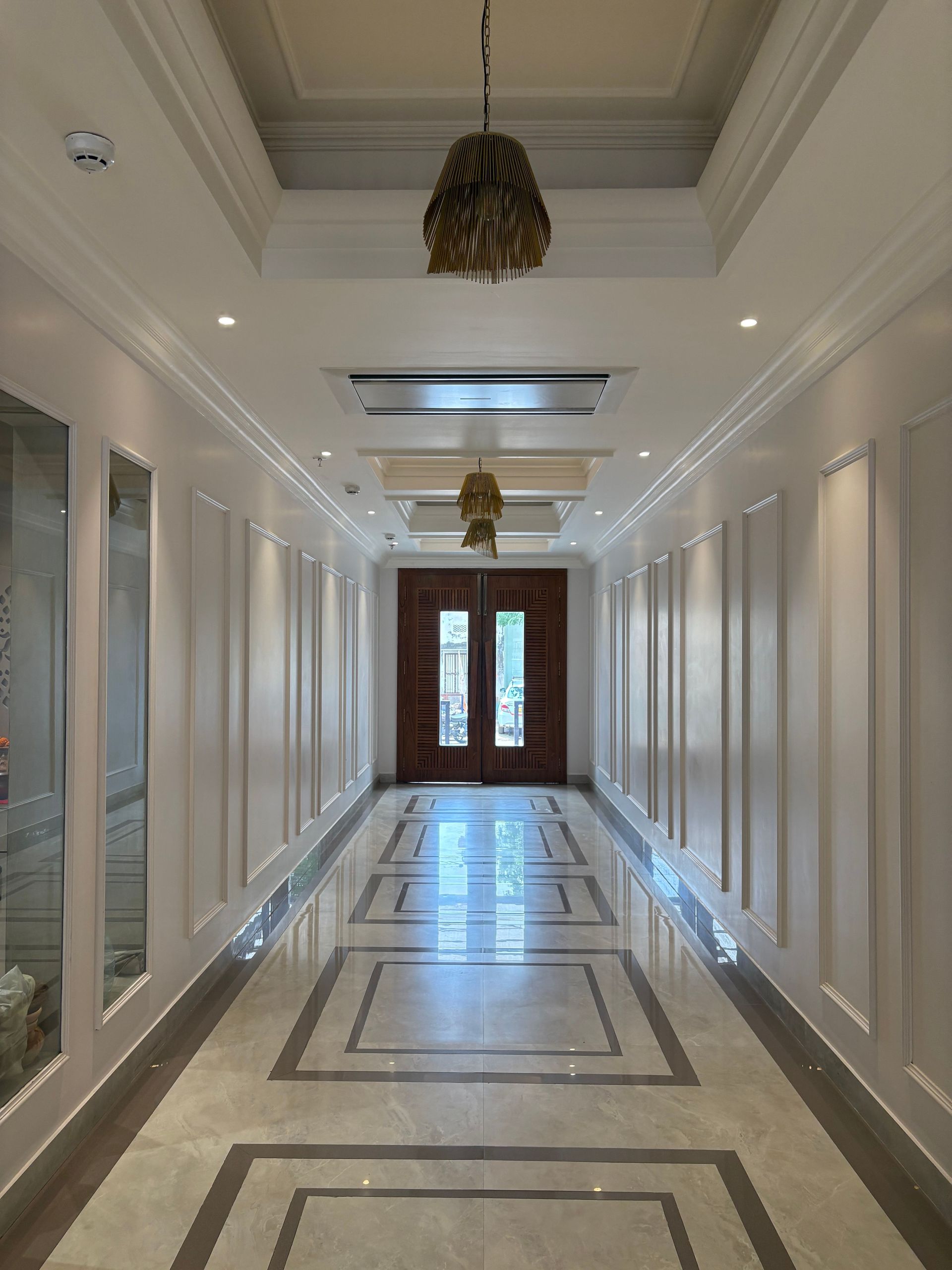 Elegant white hallway with marble floor, wall panels, and double wooden doors at the end.
