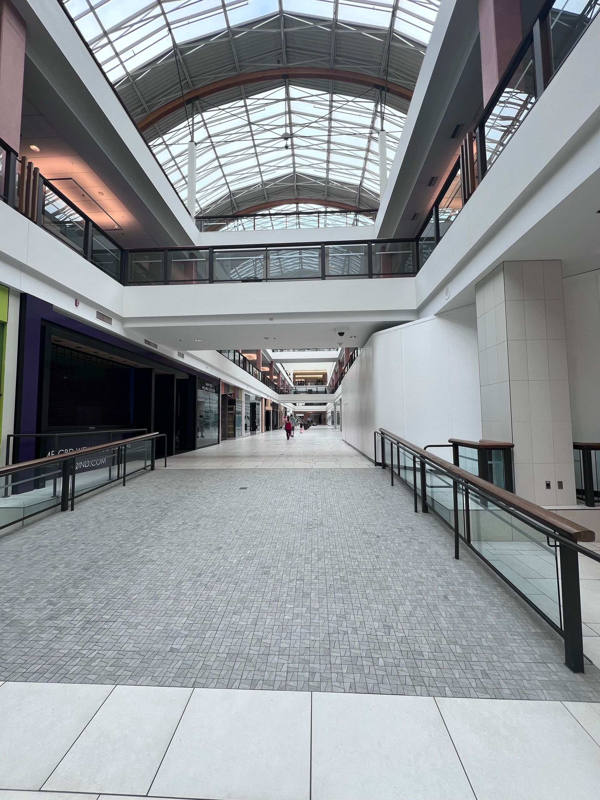 Empty indoor shopping mall corridor with a glass skylight and railings on both sides
