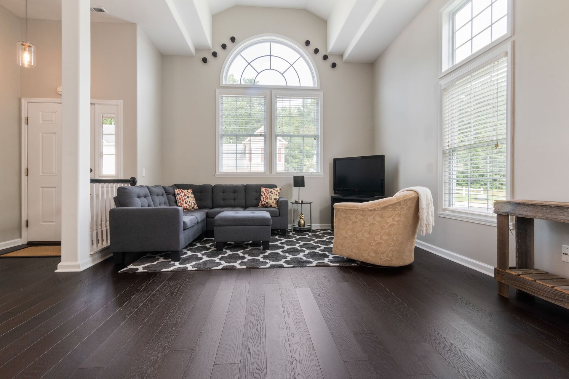 Bright modern living room with gray sectional, tan chair, large windows, and dark wood floors