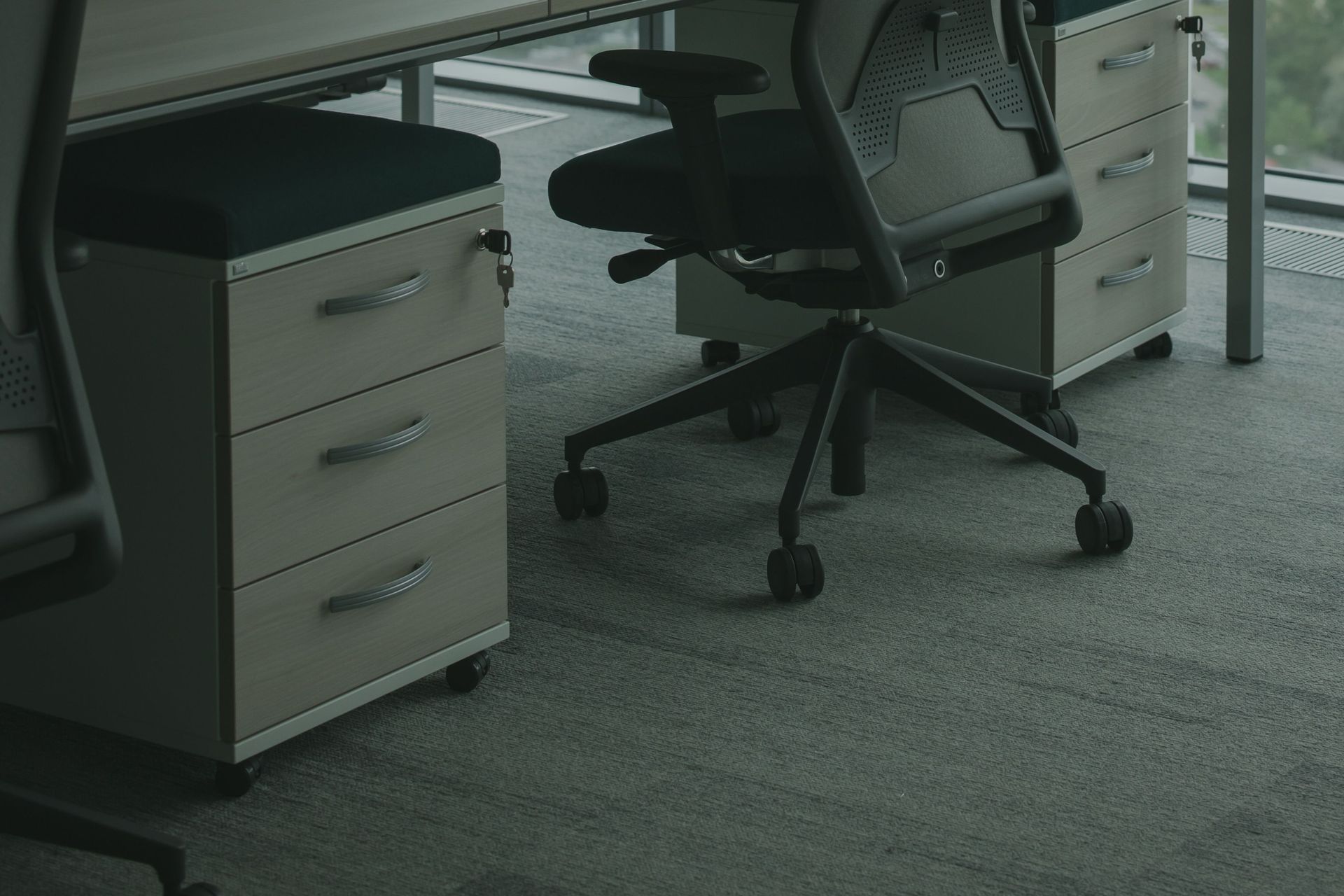Office desk with drawers and a black swivel chair on a gray carpet floor