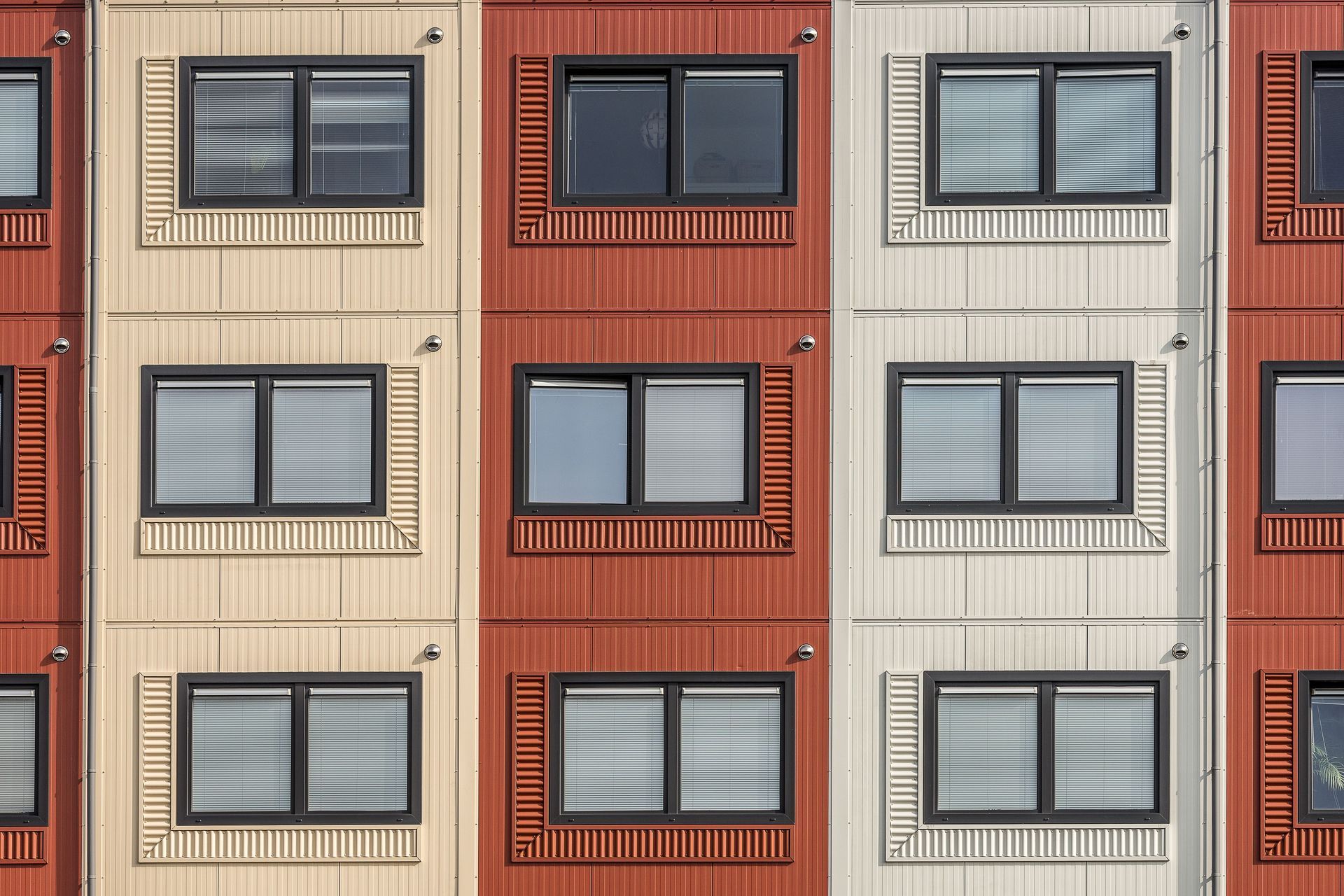 Apartment building facade with beige, rust red, and white panels and rows of windows
