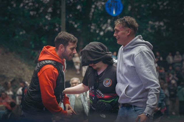 Trois personnes à l'extérieur, souriantes et discutant, l'une portant une veste orange et l'autre un sweat à capuche gris.