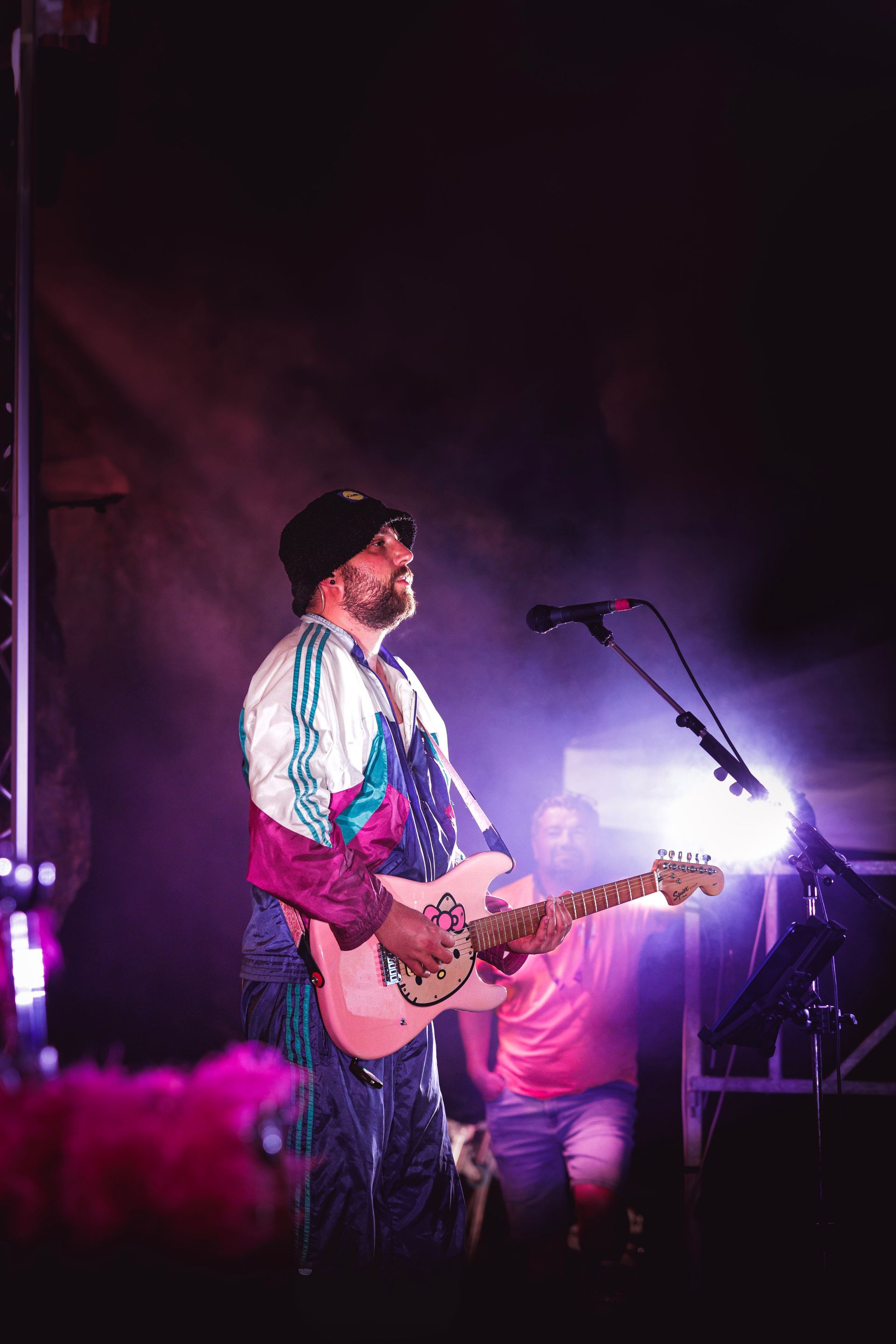 Un chanteur joue de la guitare sur une scène enfumée, sous des lumières violettes et blanches.