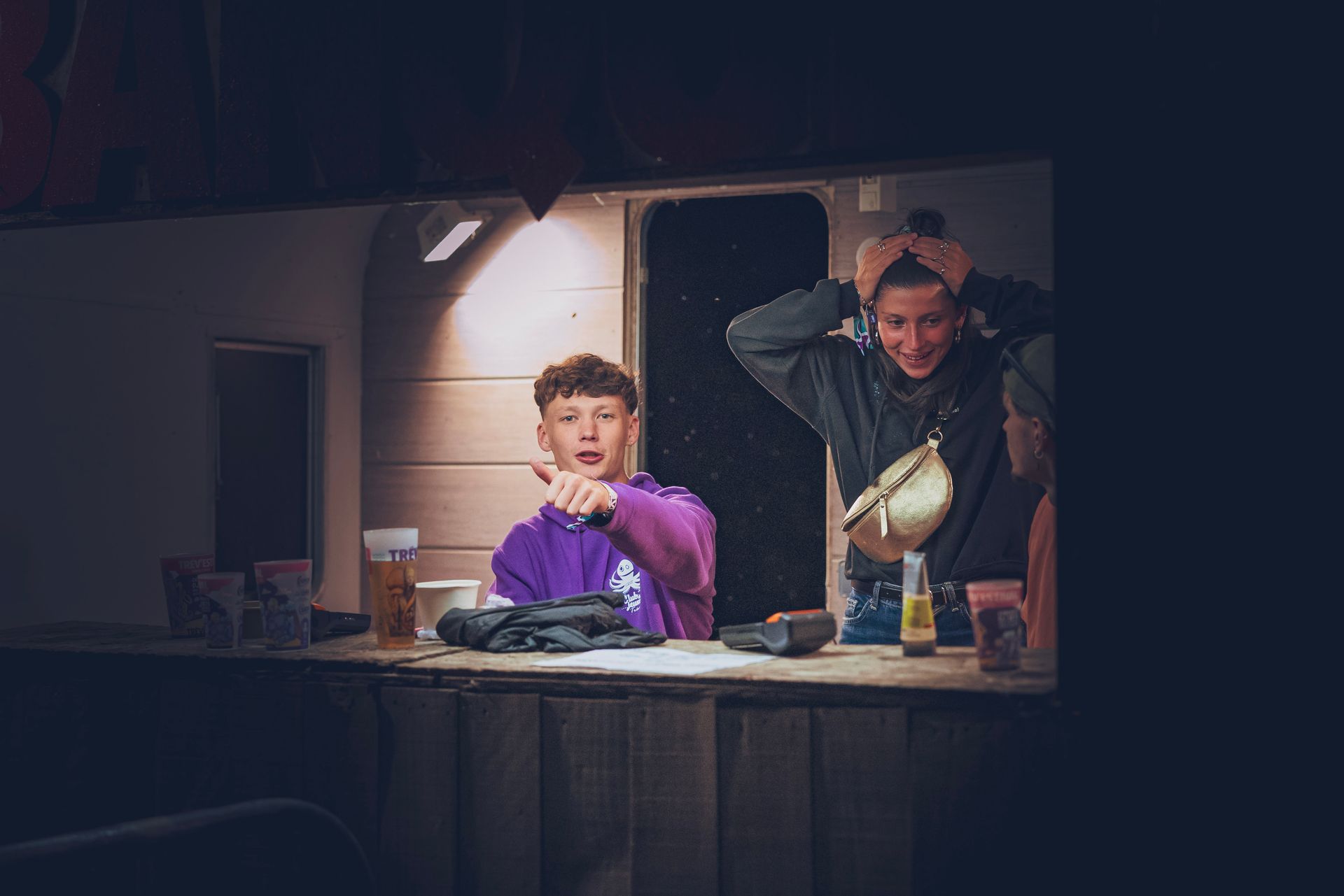Deux personnes assises à un comptoir dans une cuisine faiblement éclairée, l'une vêtue de violet et l'autre de noir, sous une douce lumière suspendue.