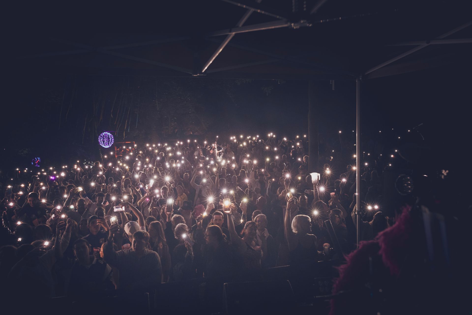 Foule à un concert dans l'obscurité, de nombreux téléphones portables brillent sous le chapiteau de la scène.