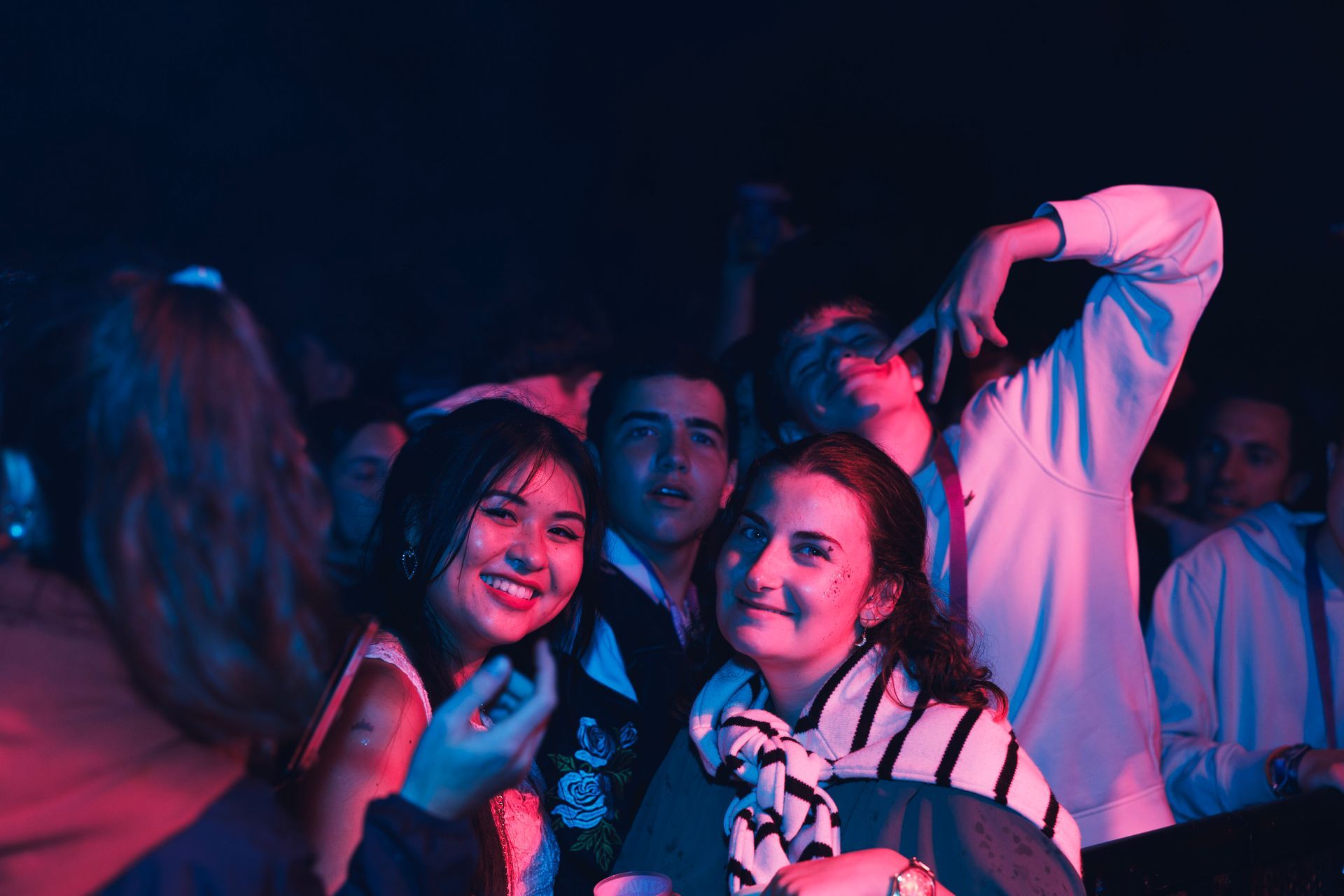 Des gens sourient dans une foule éclairée au néon lors d'une fête ou d'un concert dans l'obscurité.