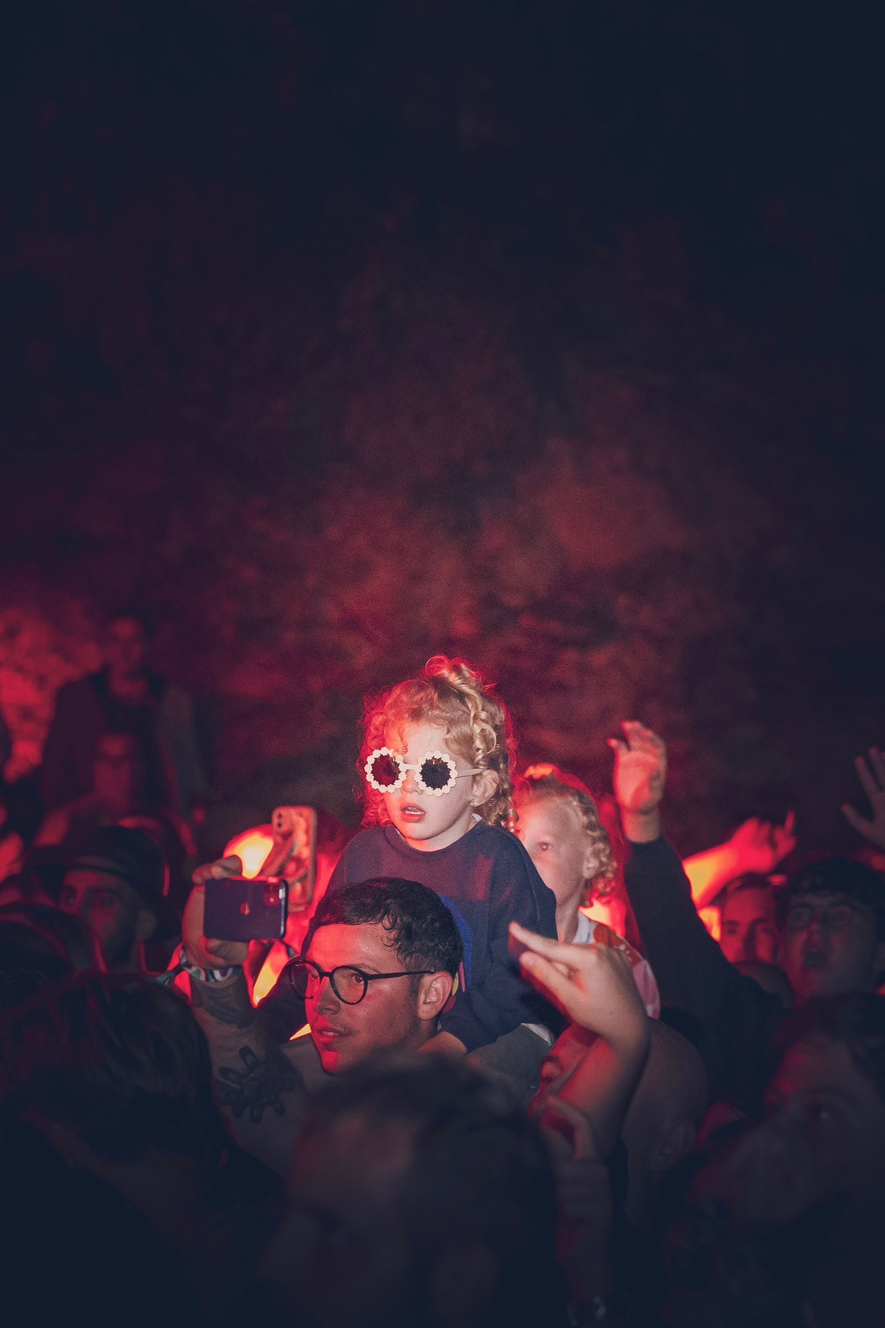 Une personne portant des lunettes de soleil au milieu d'une foule éclairée en rouge lors d'un concert ou d'une fête