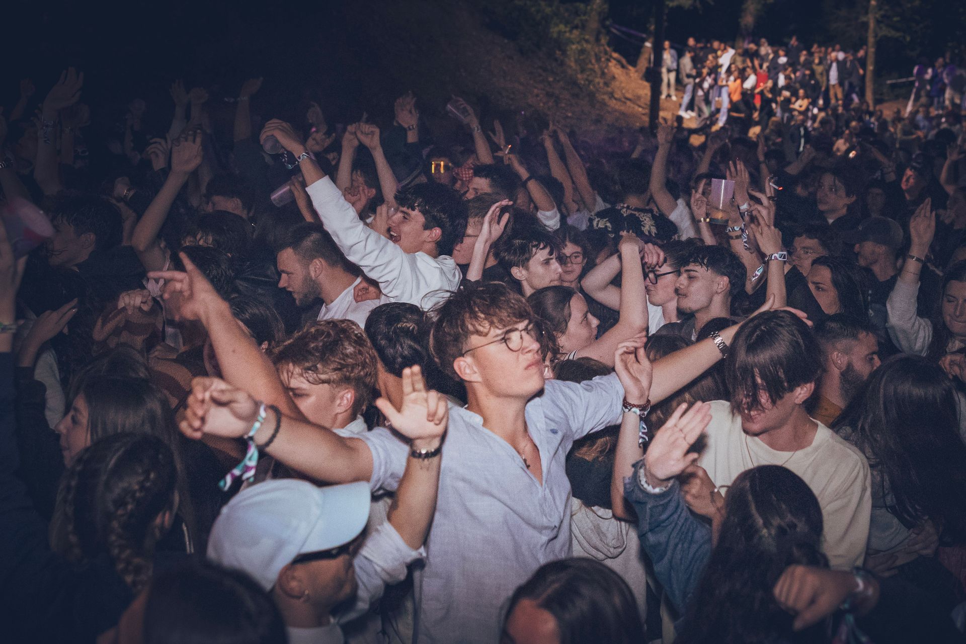 La foule danse lors d'un concert nocturne, les mains levées sous les lumières colorées de la scène