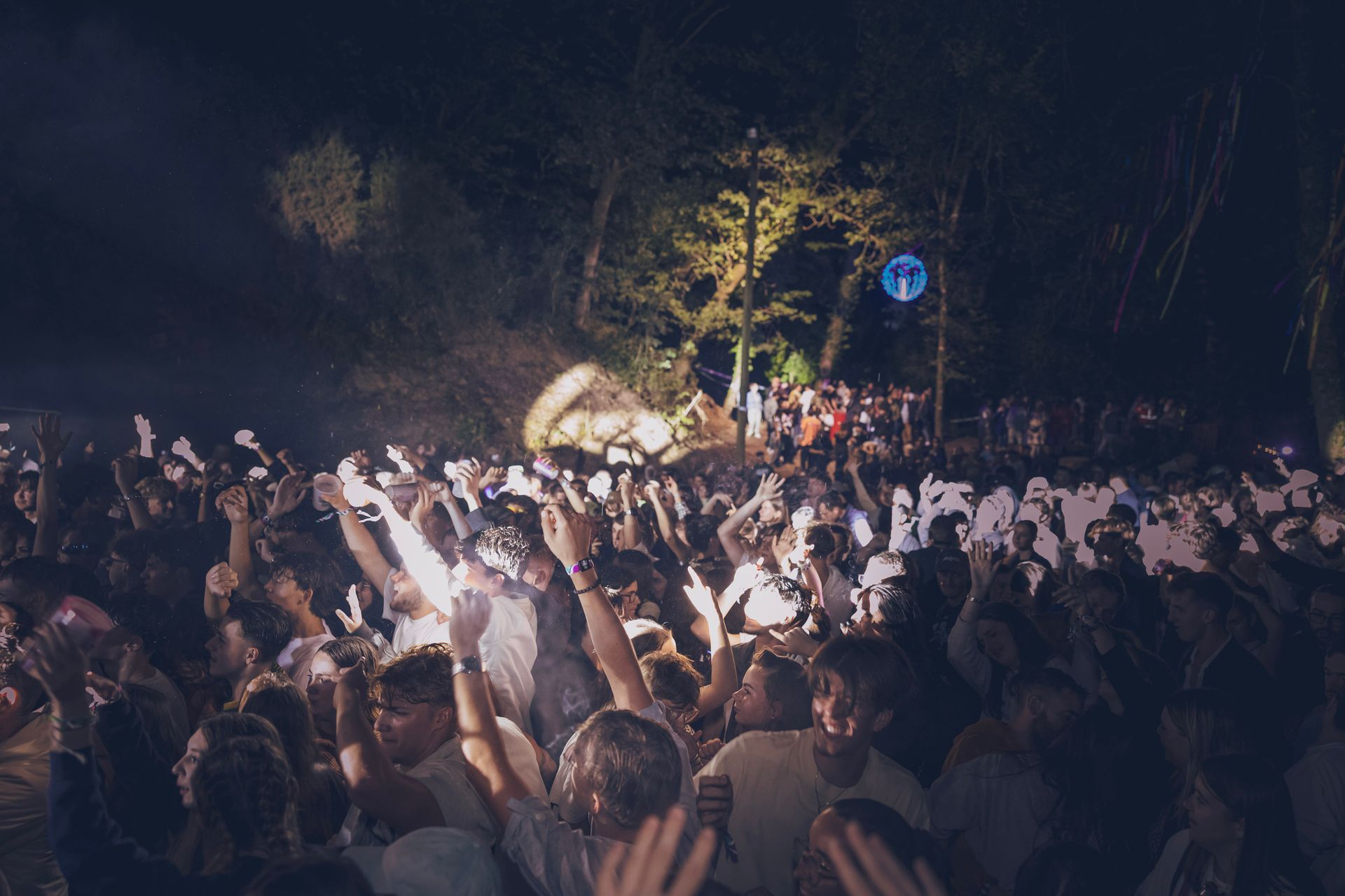 Foule dense à un concert nocturne, les mains levées sous les projecteurs et les arbres à proximité