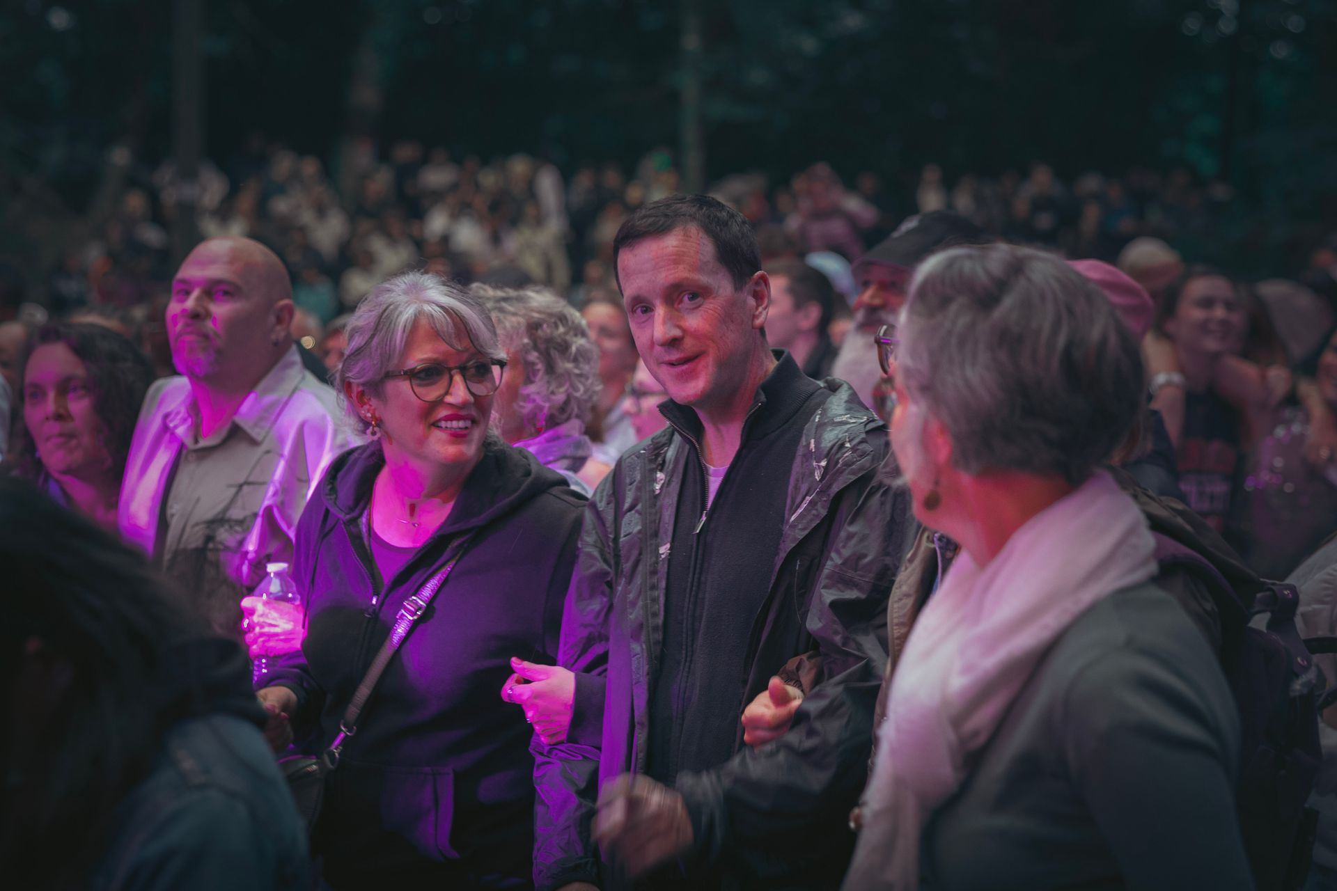 Des spectateurs assis lors d'un événement, une personne souriant sous une lumière de scène violette