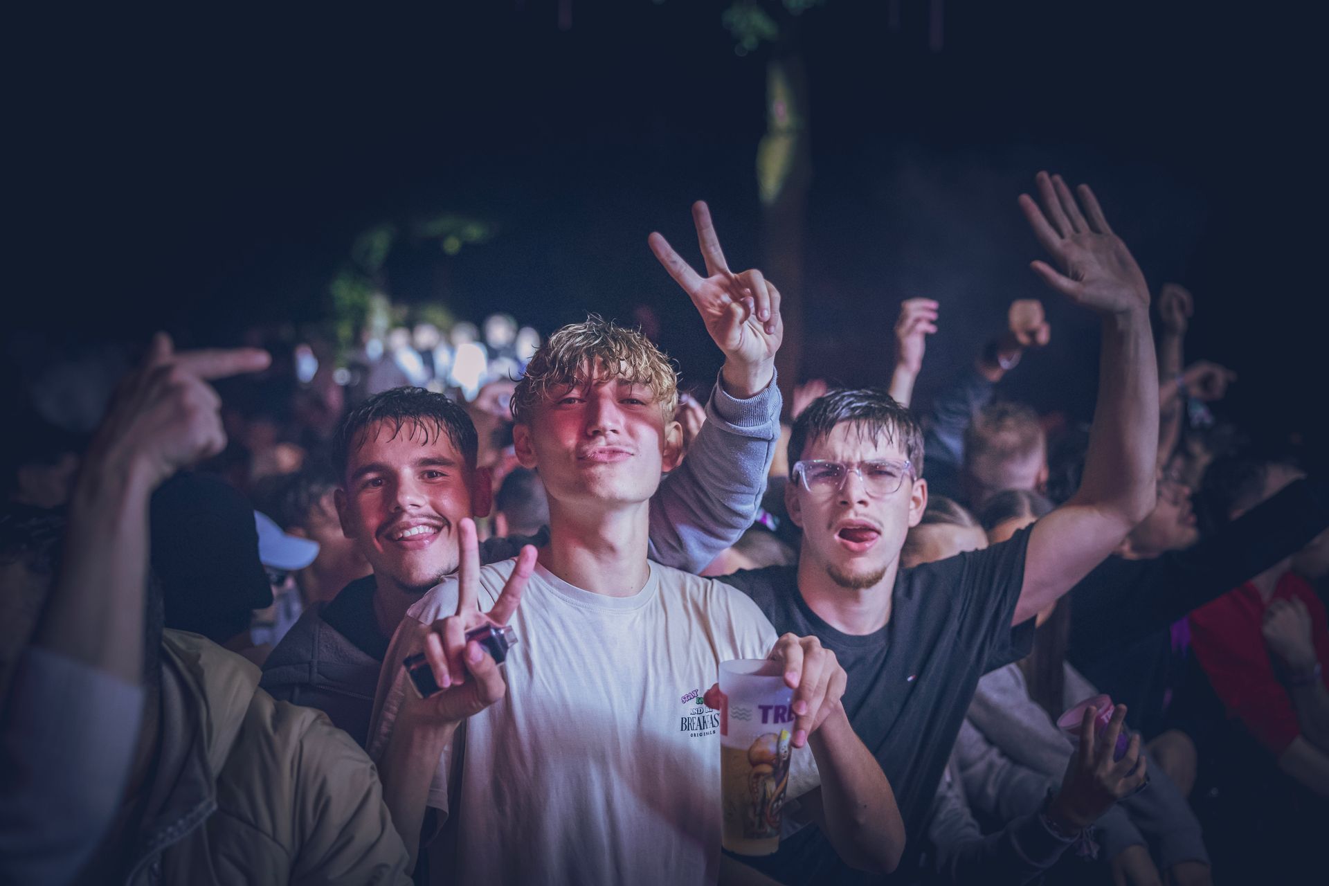 La foule, lors d'un concert, acclame et lève les mains sous les projecteurs ; une personne fait le signe de la paix.