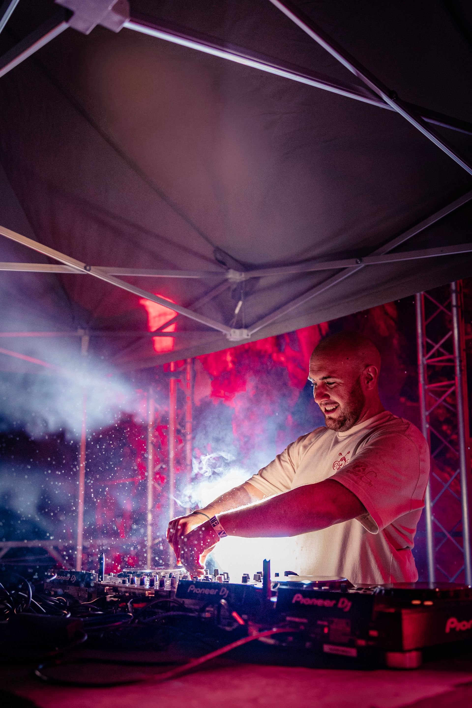 Un DJ mixe sous une tente, entouré de lumières rouges et bleues et de fumée.