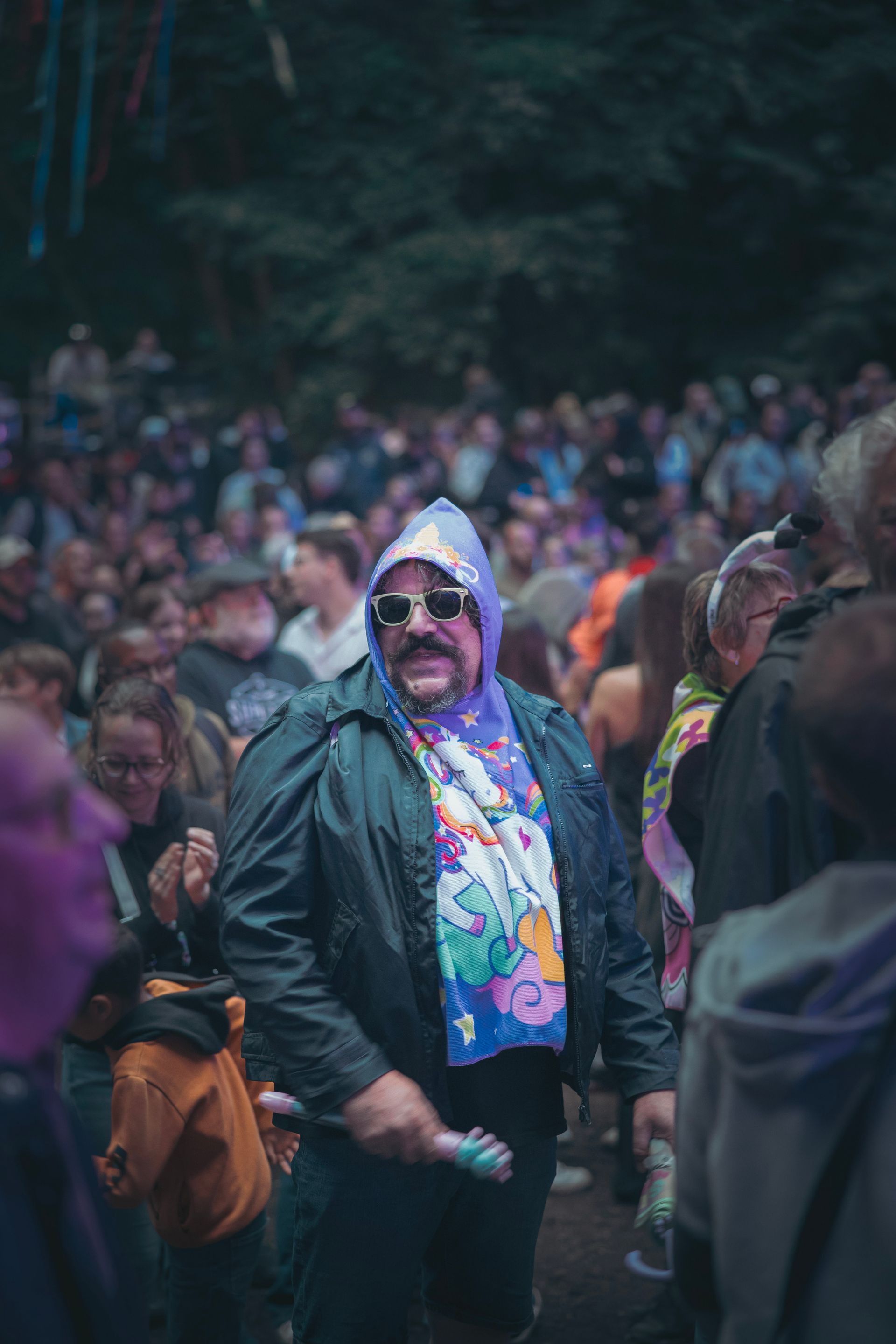 Une personne portant des lunettes de soleil et une écharpe colorée se tient devant une foule nombreuse à l'extérieur.