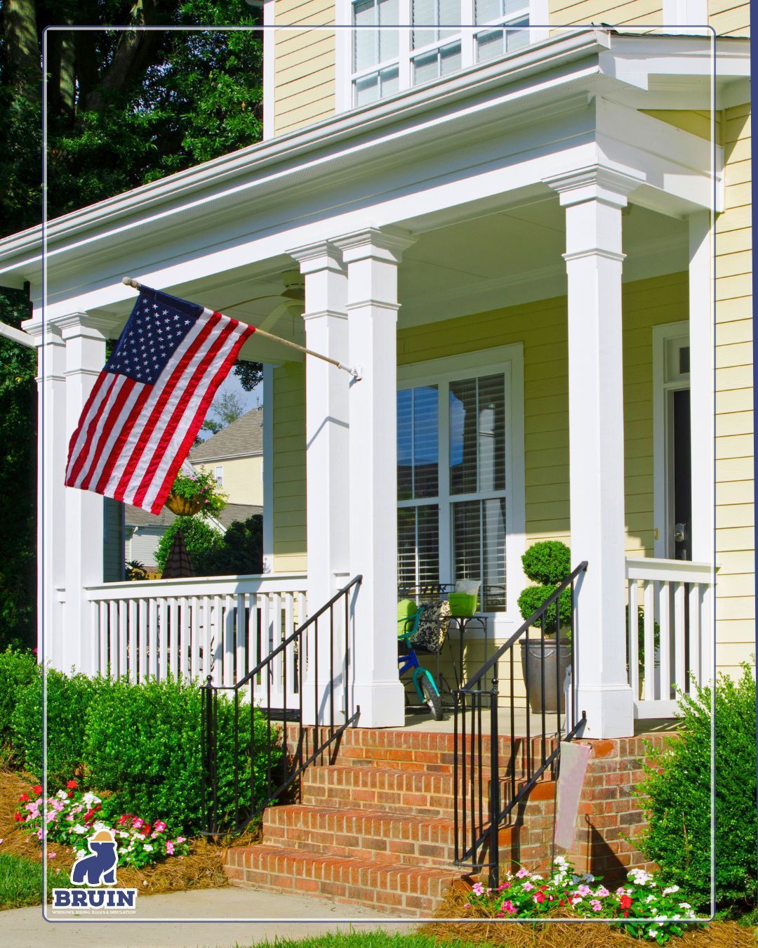 Front porch with white columns, brick steps, potted plants, and an American flag hanging by the entrance.