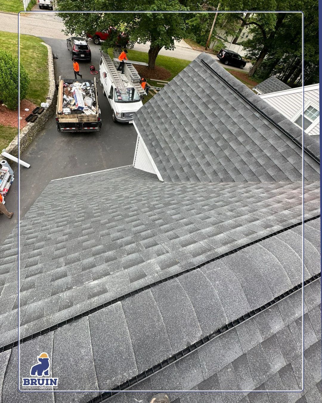 Roof shingles in foreground with two utility trucks and workers below on a residential street
