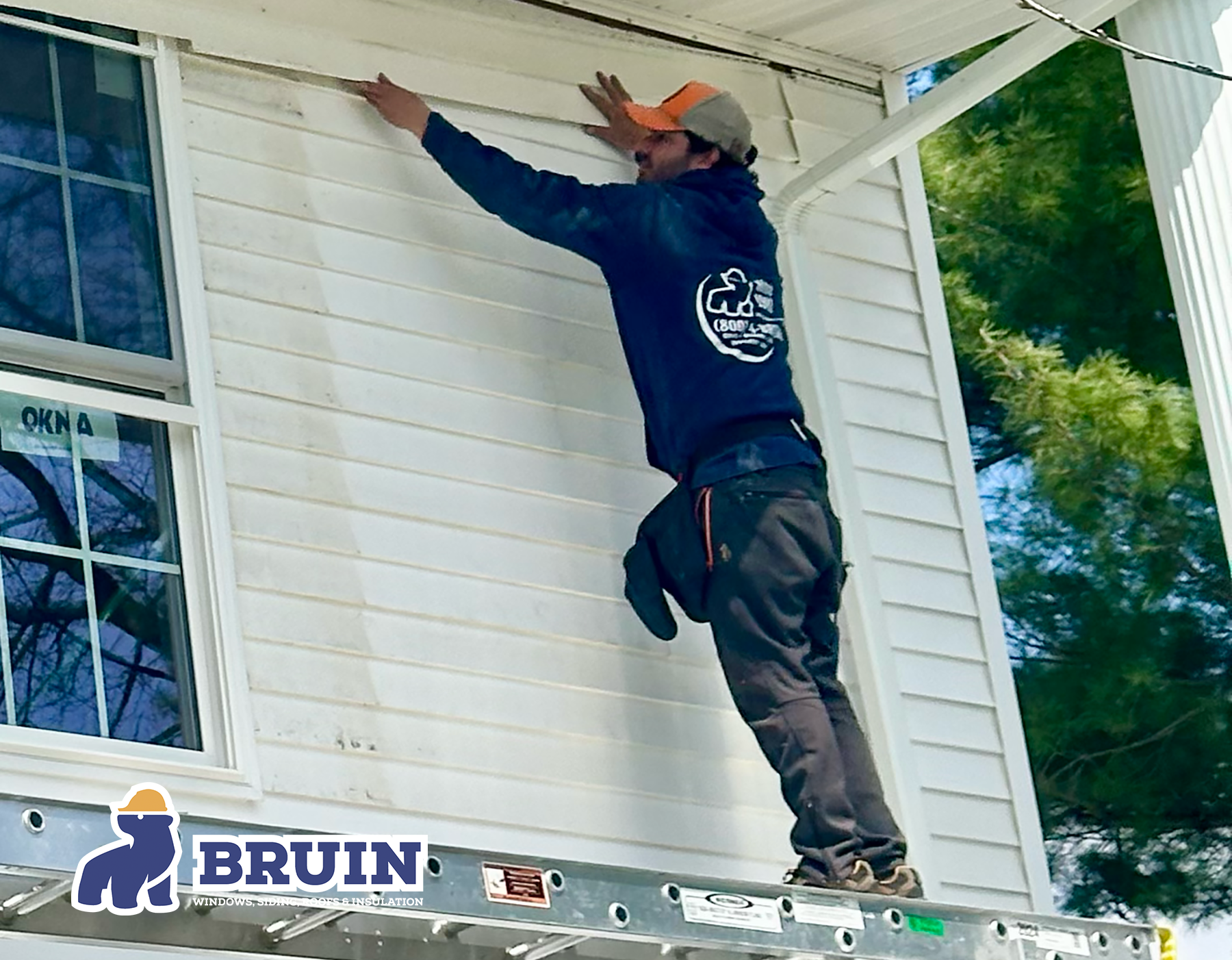 Worker on a ladder painting white house trim under a porch roof
