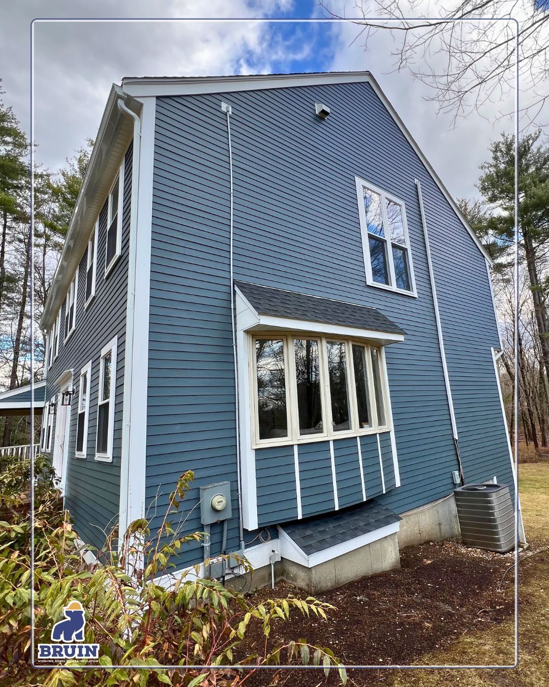 Blue two-story house with white-trim windows and a small covered porch, viewed from the side.