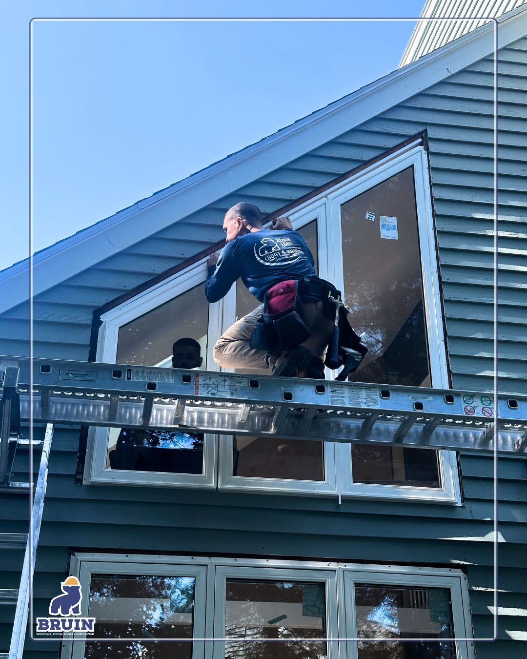Two workers on a metal scaffold repairing a house’s roof beside a brown door and blue siding