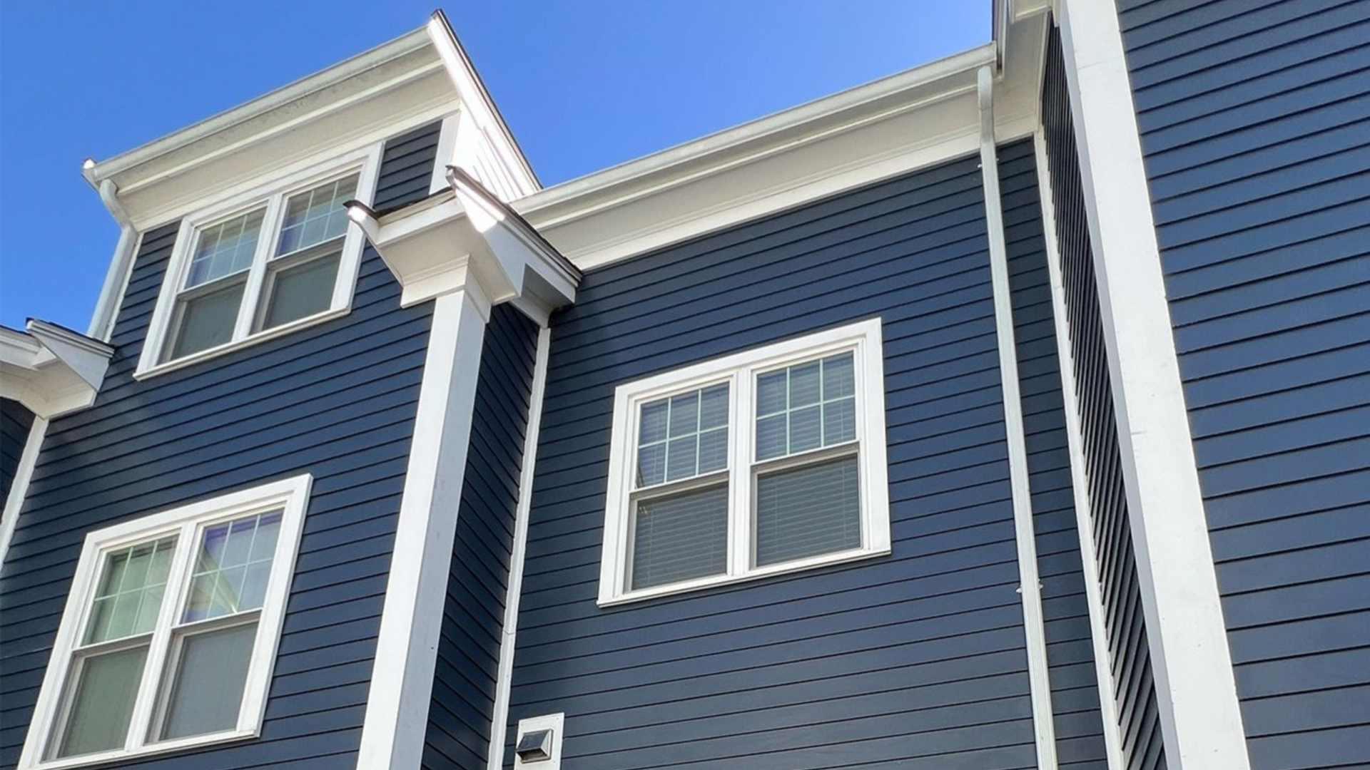 Blue house exterior with white trim and windows, viewed from below against the sky