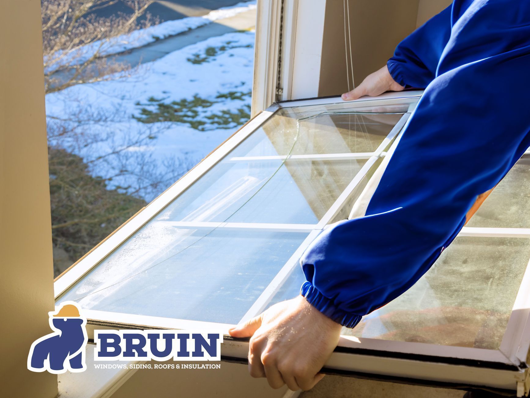 Person carrying a window frame indoors, with snow visible outside and a BRUIN logo in the corner