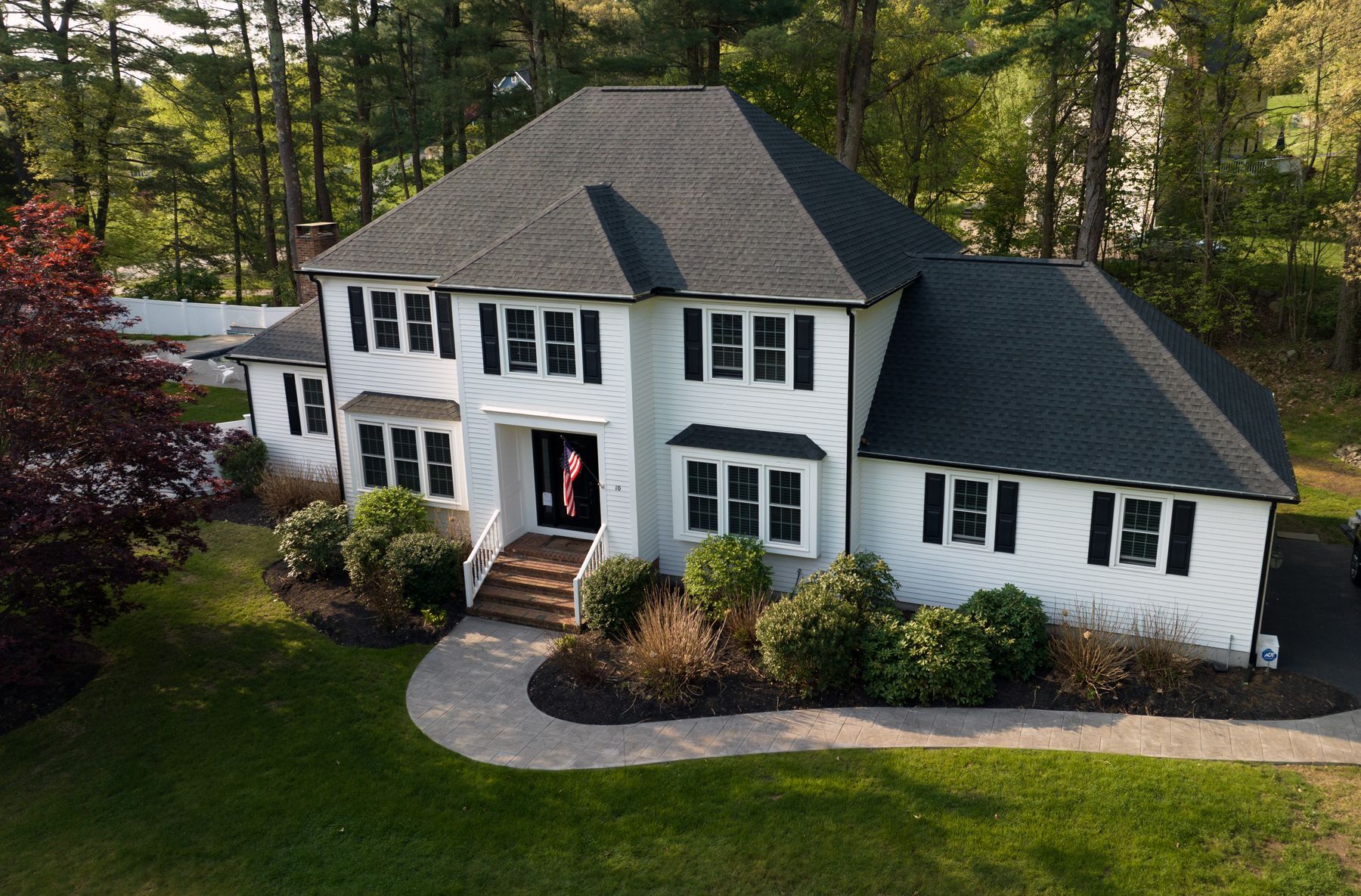 An aerial view of a large white house with a black roof surrounded by trees.