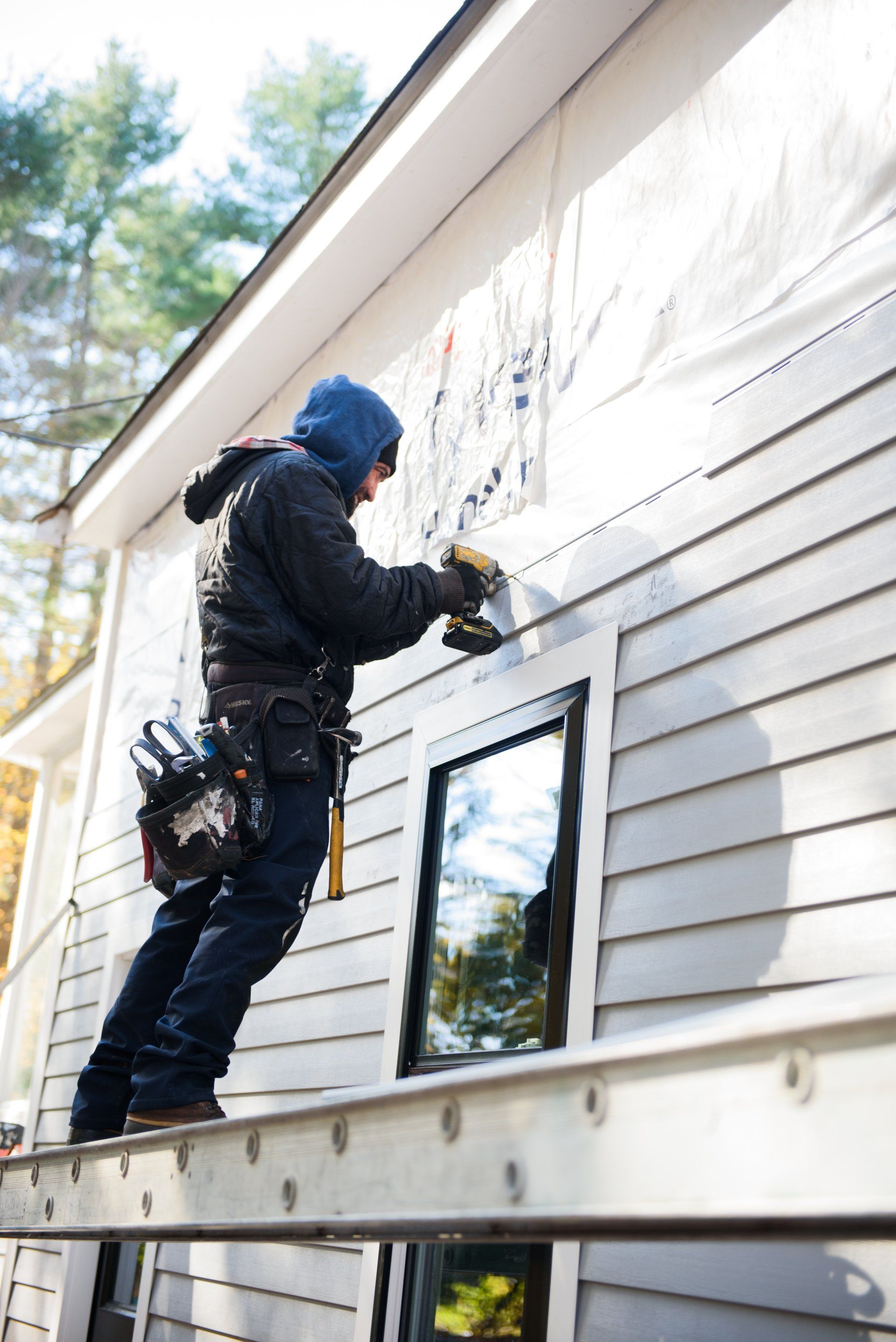 A man is standing on a ladder working on the side of a house.