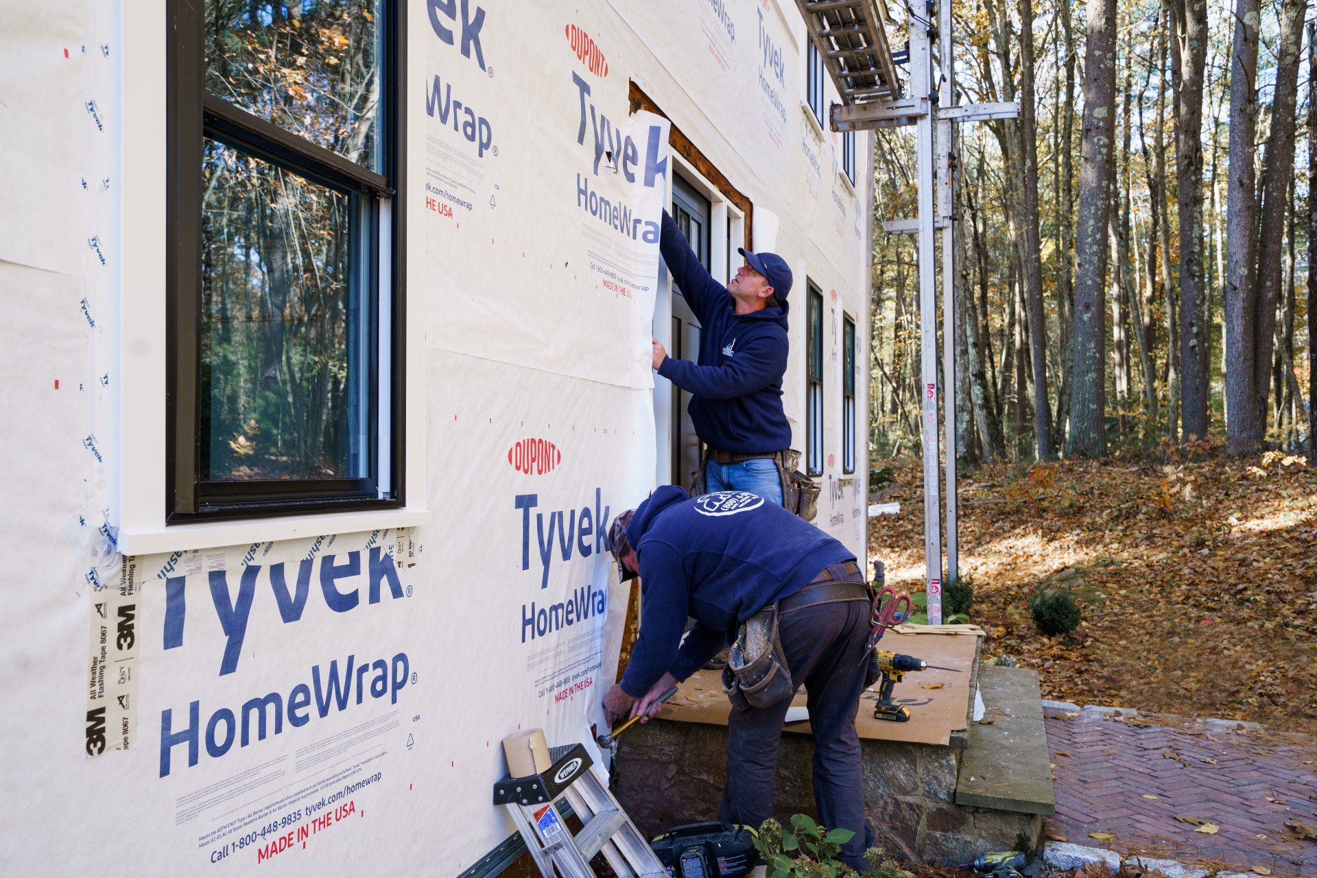 Two men are working on the side of a house with a ladder.