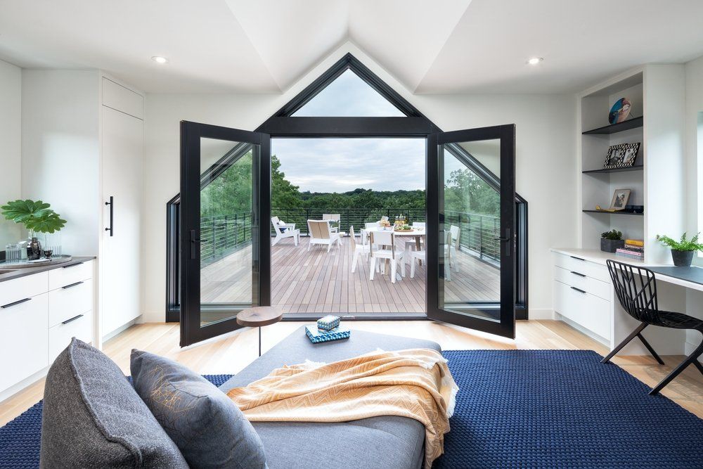 A living room with a couch and a desk and a view of a deck.