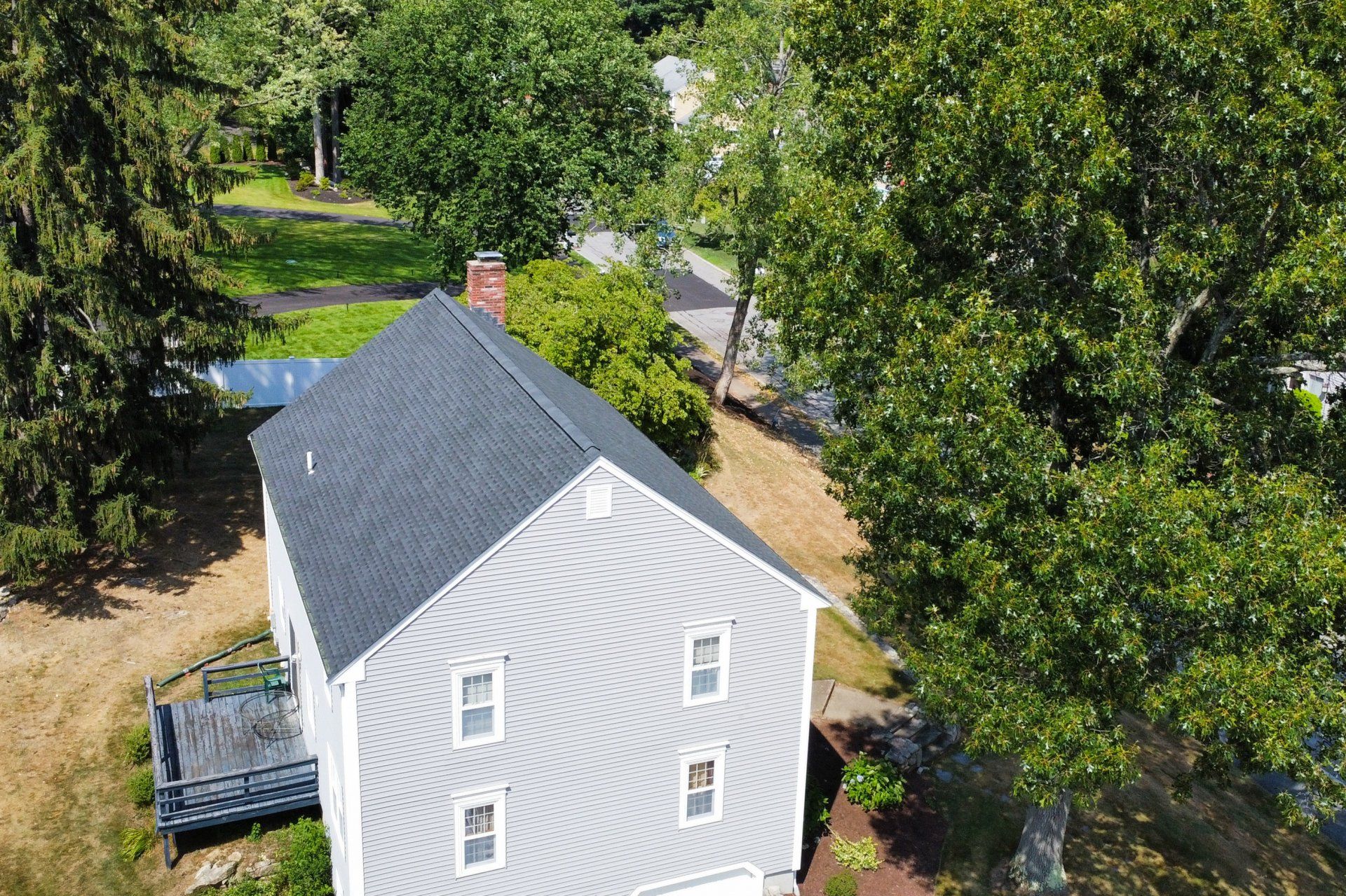 An aerial view of a white house with a black roof surrounded by trees.