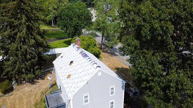 An aerial view of a house with a roof being installed surrounded by trees.