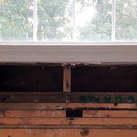A wooden wall with a hole in it and a window in the background.