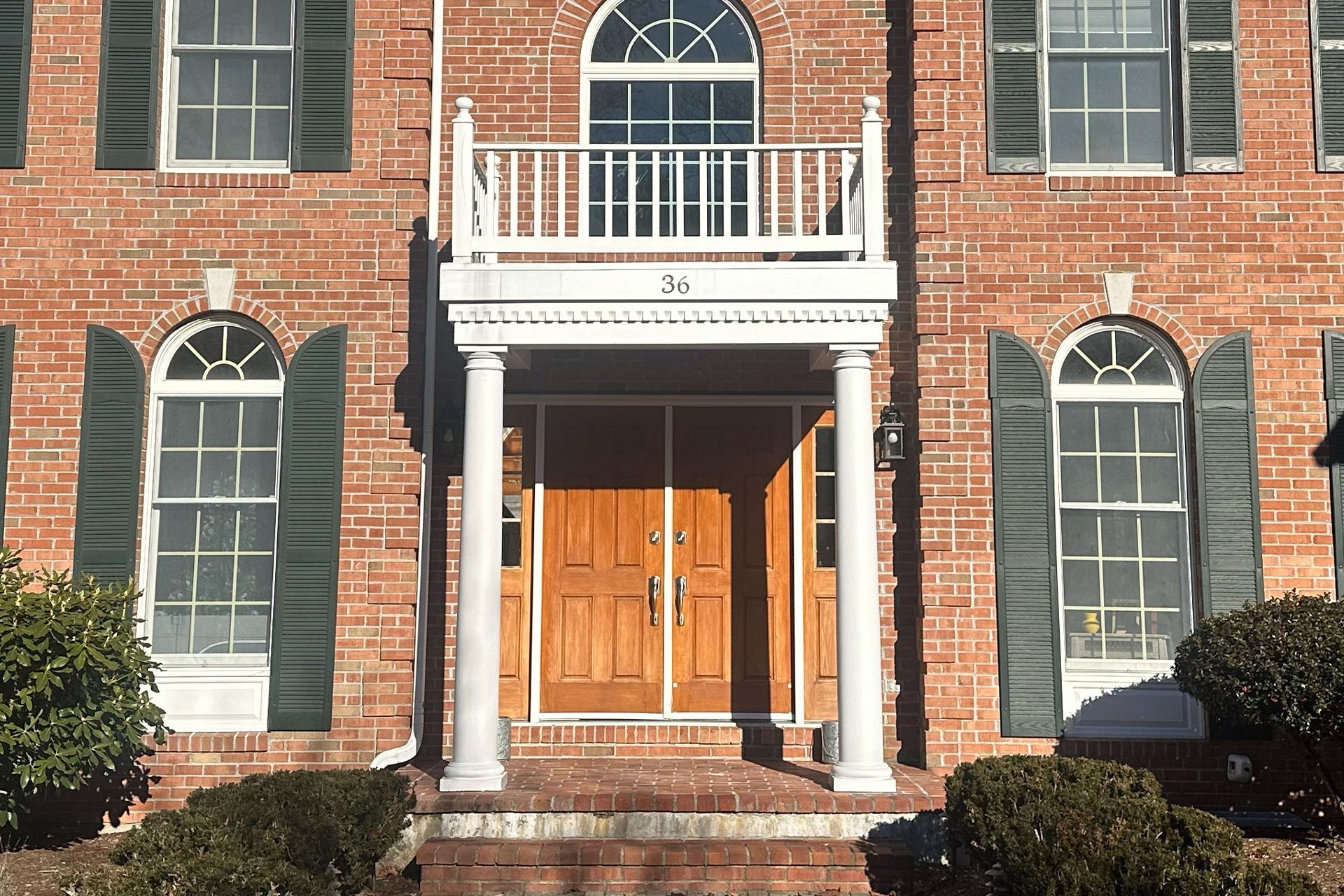Brick house facade with white columns, arched windows, and a wooden front door in sunlight