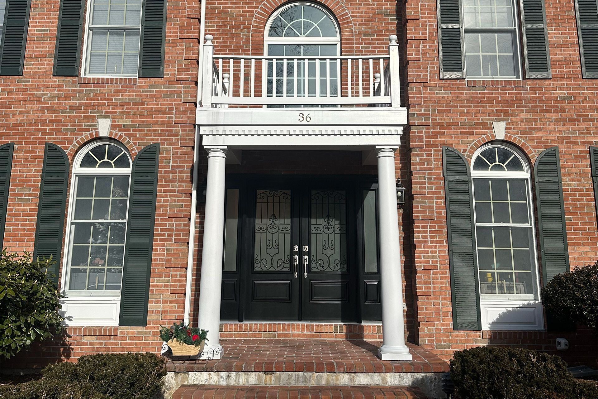 Brick house facade with white columns, arched windows, and a black double front door