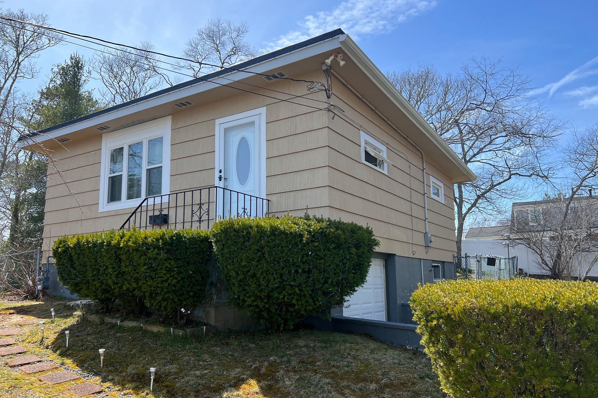 Small beige house with white trim and trimmed hedges in a sunny yard