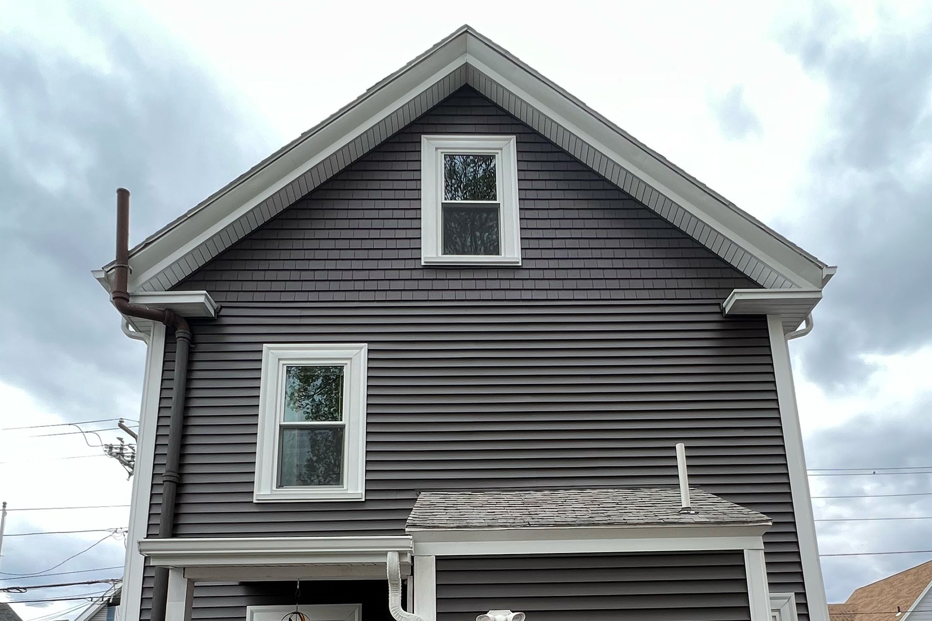 Dark gray house with white trim and a gabled roof under cloudy sky