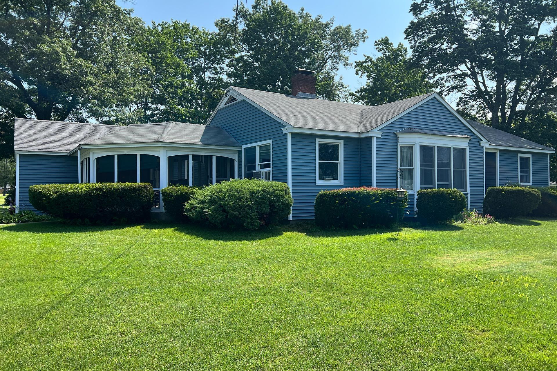 Blue single-story house with white trim, front bushes, and a green lawn under clear daylight