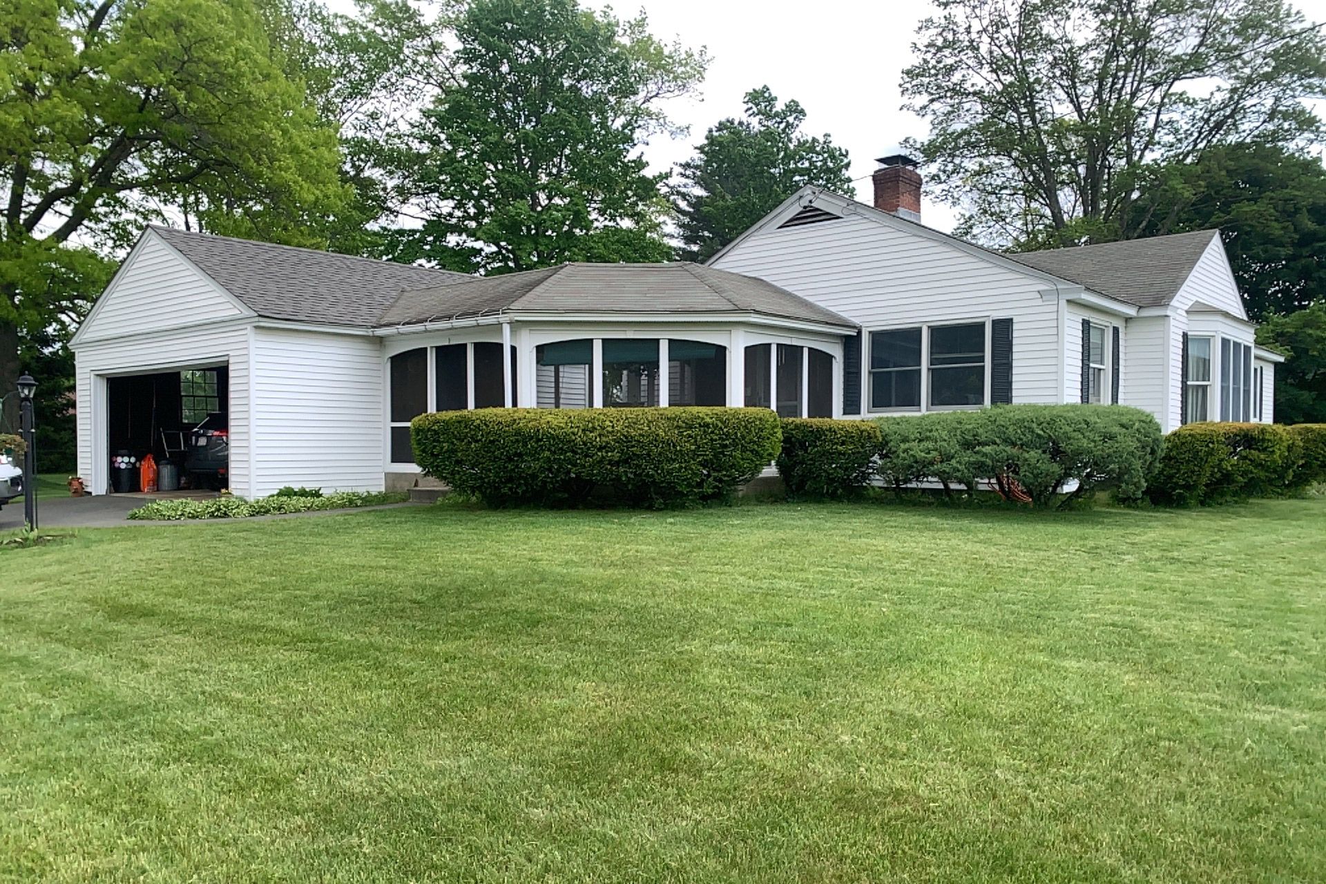 White single-story house with a detached garage, hedges, and a large green lawn