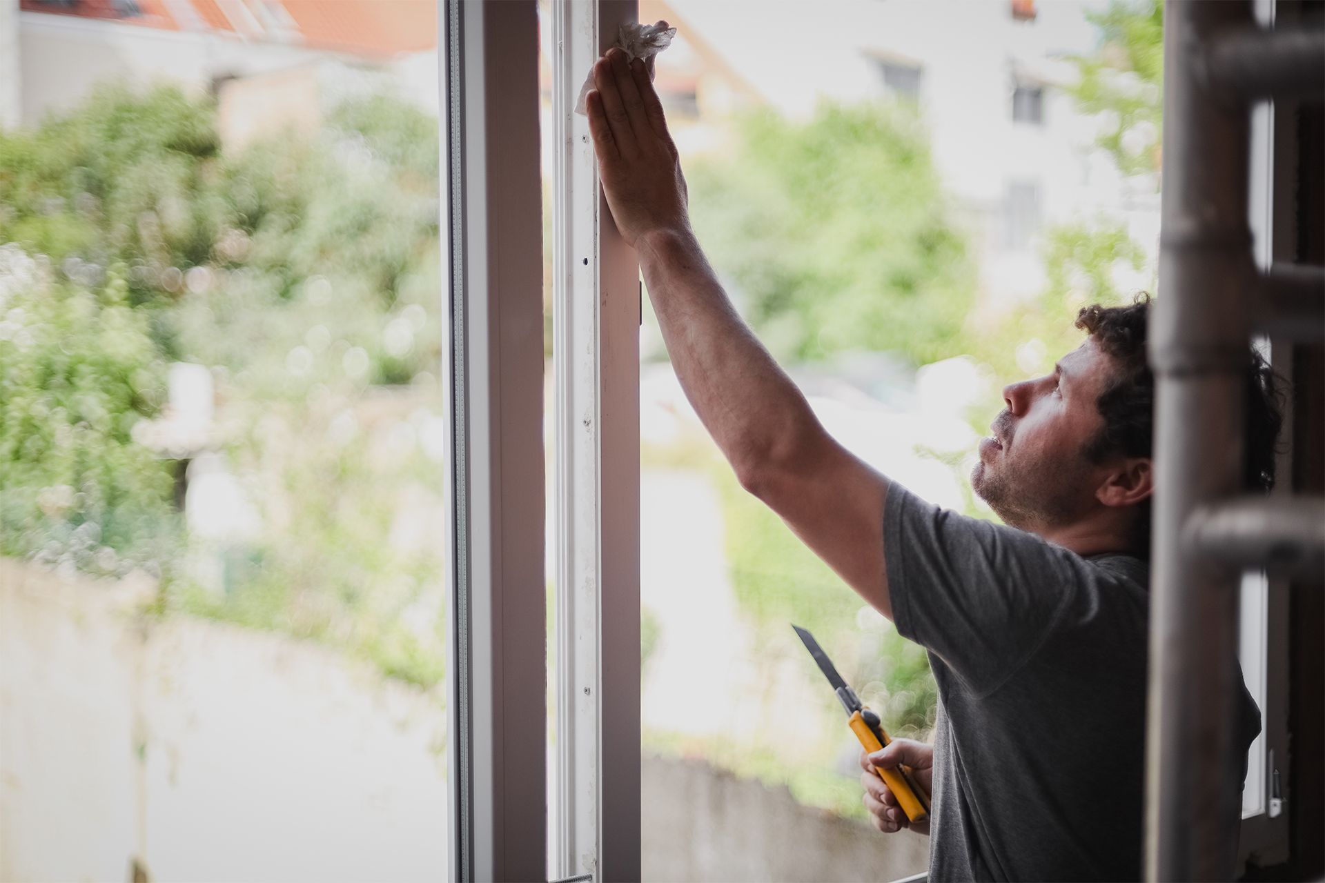 Person painting a door frame indoors with a brush, near an open window.