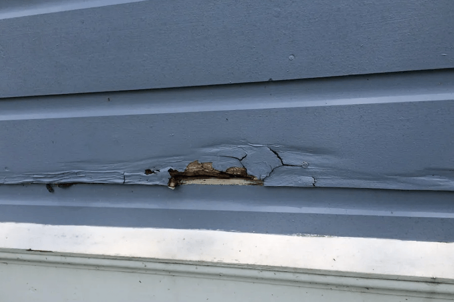 A close up of a blue siding on a house with a hole in it.