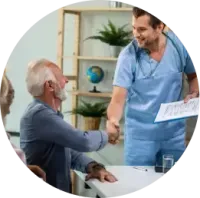 Doctor in blue scrubs shaking hands with a seated patient in a clinic office