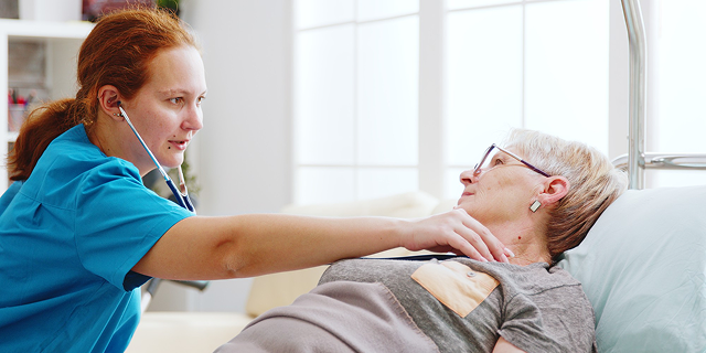 Nurse checking an elderly patient in a hospital bed with a stethoscope