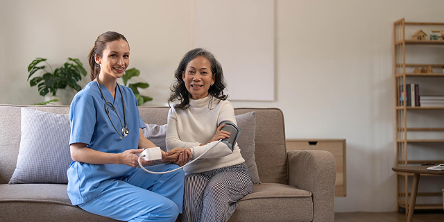 Two women sit on a couch in a bright living room, smiling and reviewing papers together.