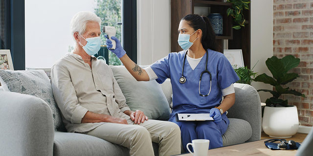 Nurse checks an elderly patient’s temperature with a forehead scanner in a home setting